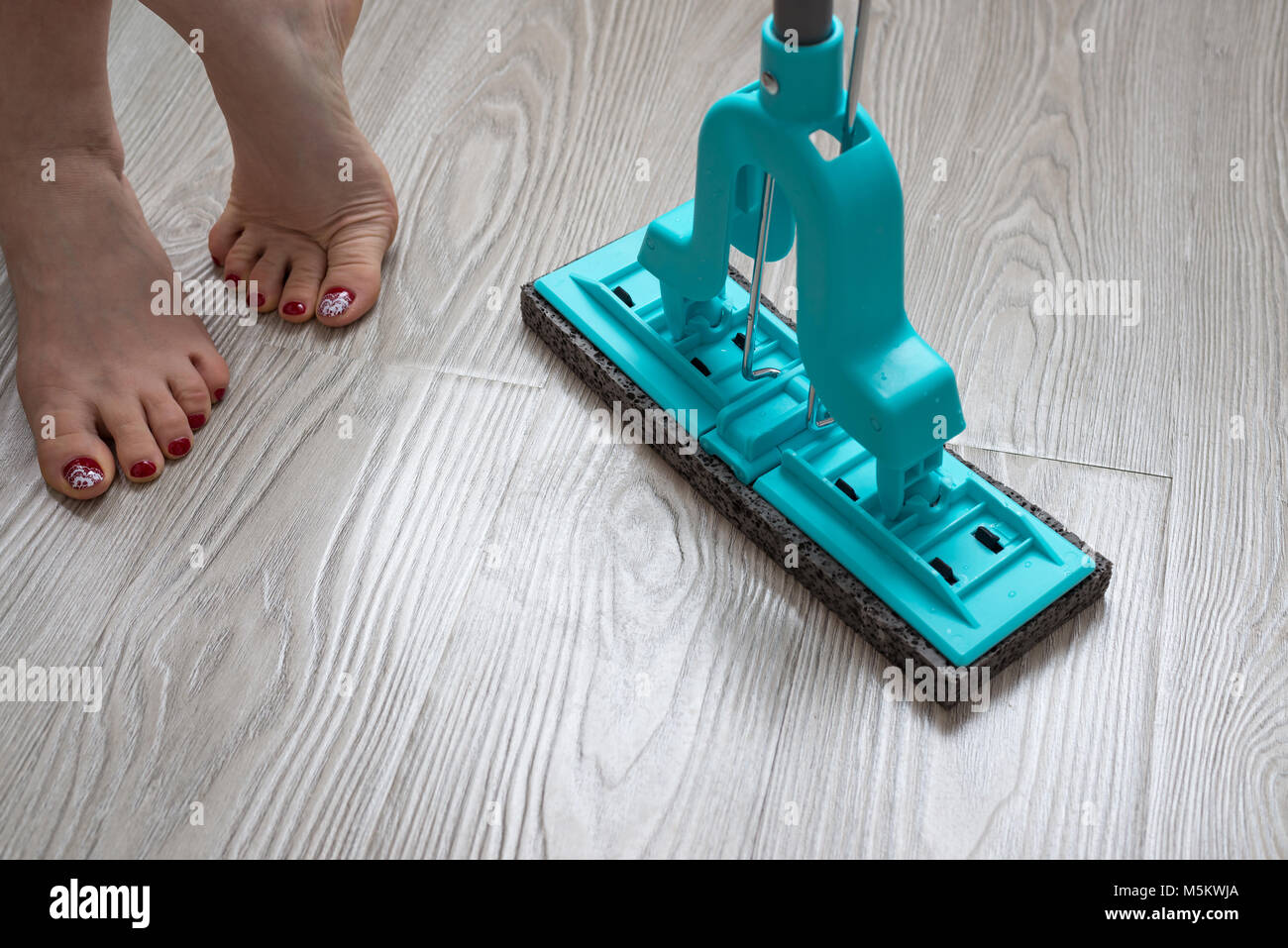 Weibliche Füße und Blau mop auf Laminat Hintergrund Stockfoto