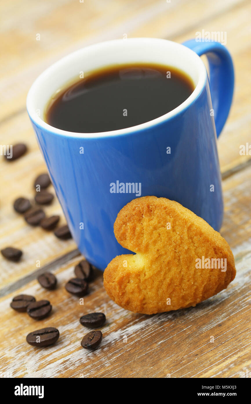 Herzförmige cookie lehnte sich gegen die Tasse Kaffee auf Holzmöbeln im Landhausstil Oberfläche Stockfoto