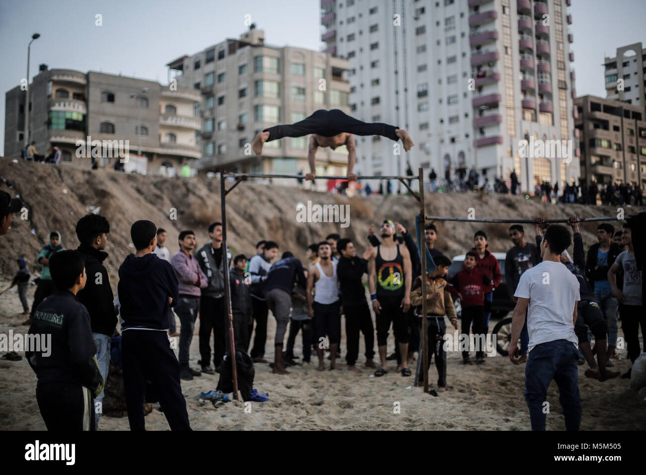 Gaza, Gaza. 23 Feb, 2018. Palästinenser beobachten, wie eine Jugend Praktiken seiner parkour Fähigkeiten auf den Strand von Gaza, Gaza, den 23. Februar 2018. Credit: Mohammed Talatene/dpa/Alamy leben Nachrichten Stockfoto