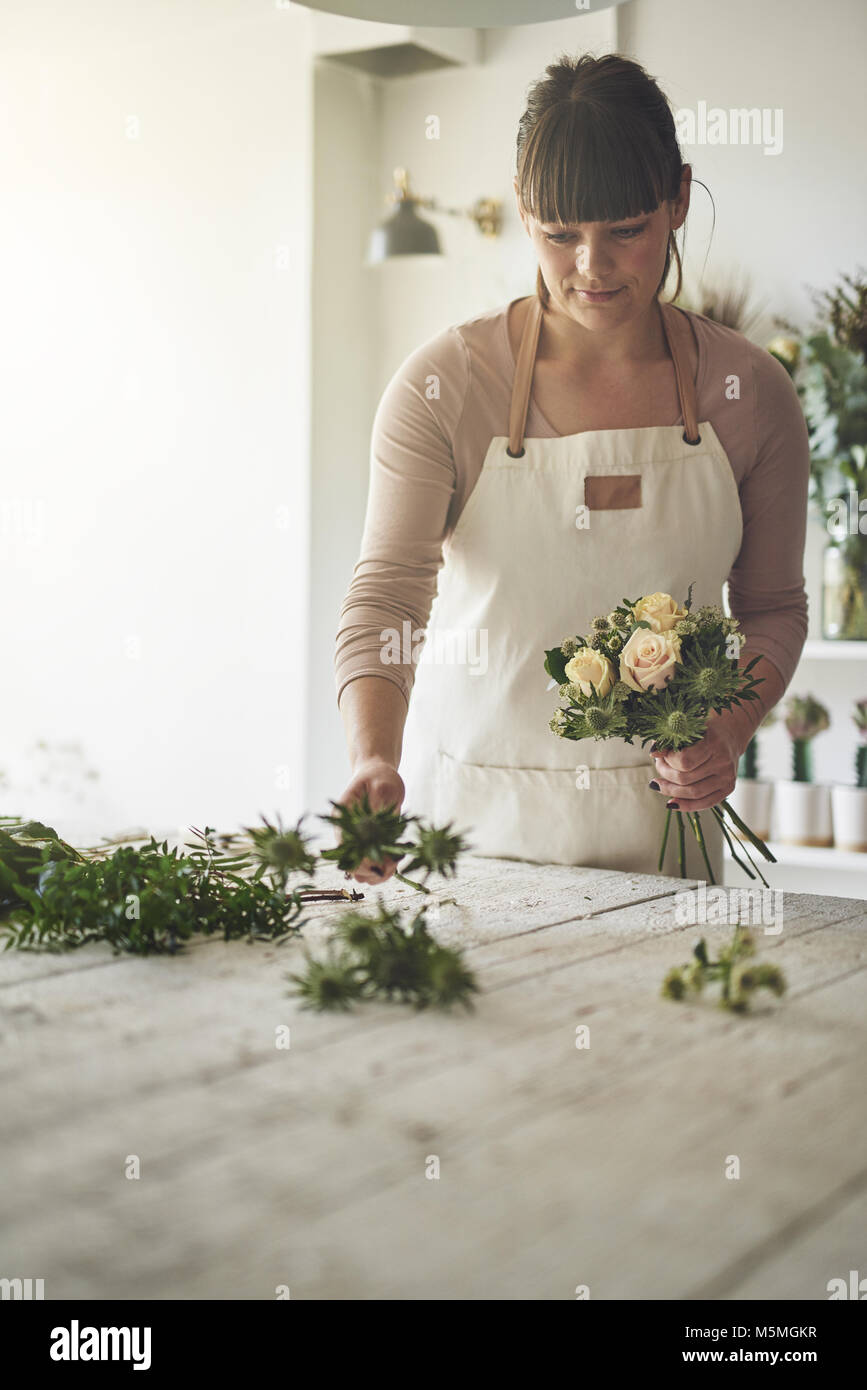 Junge weibliche Blumenhändler, der an einem Tisch in Ihrem Blumenladen zusammen mit einem Blumenstrauß aus Rosen Stockfoto