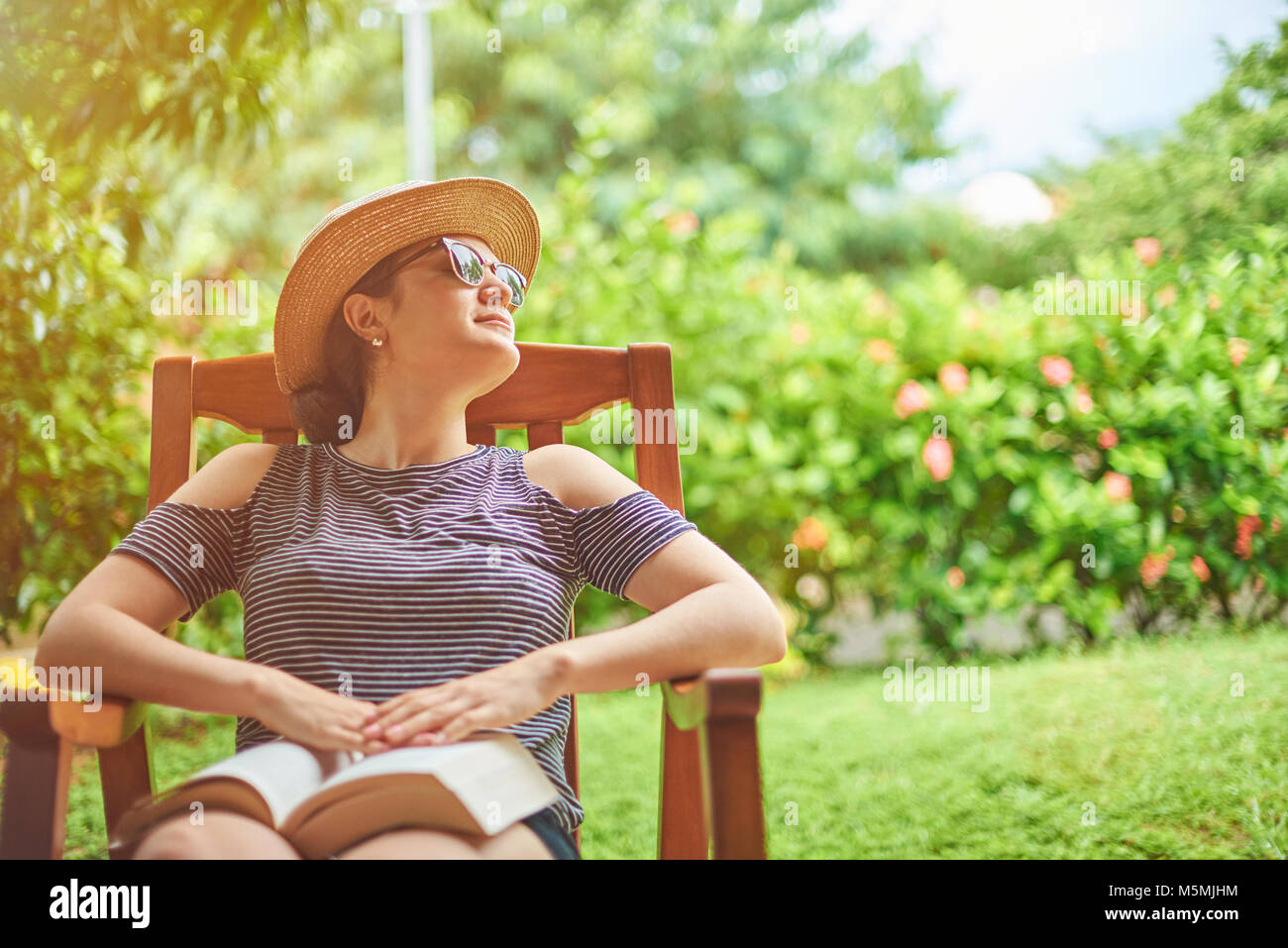 Junge Frau mit Buch sitzen auf Stuhl im grünen Garten Terrasse Stockfoto