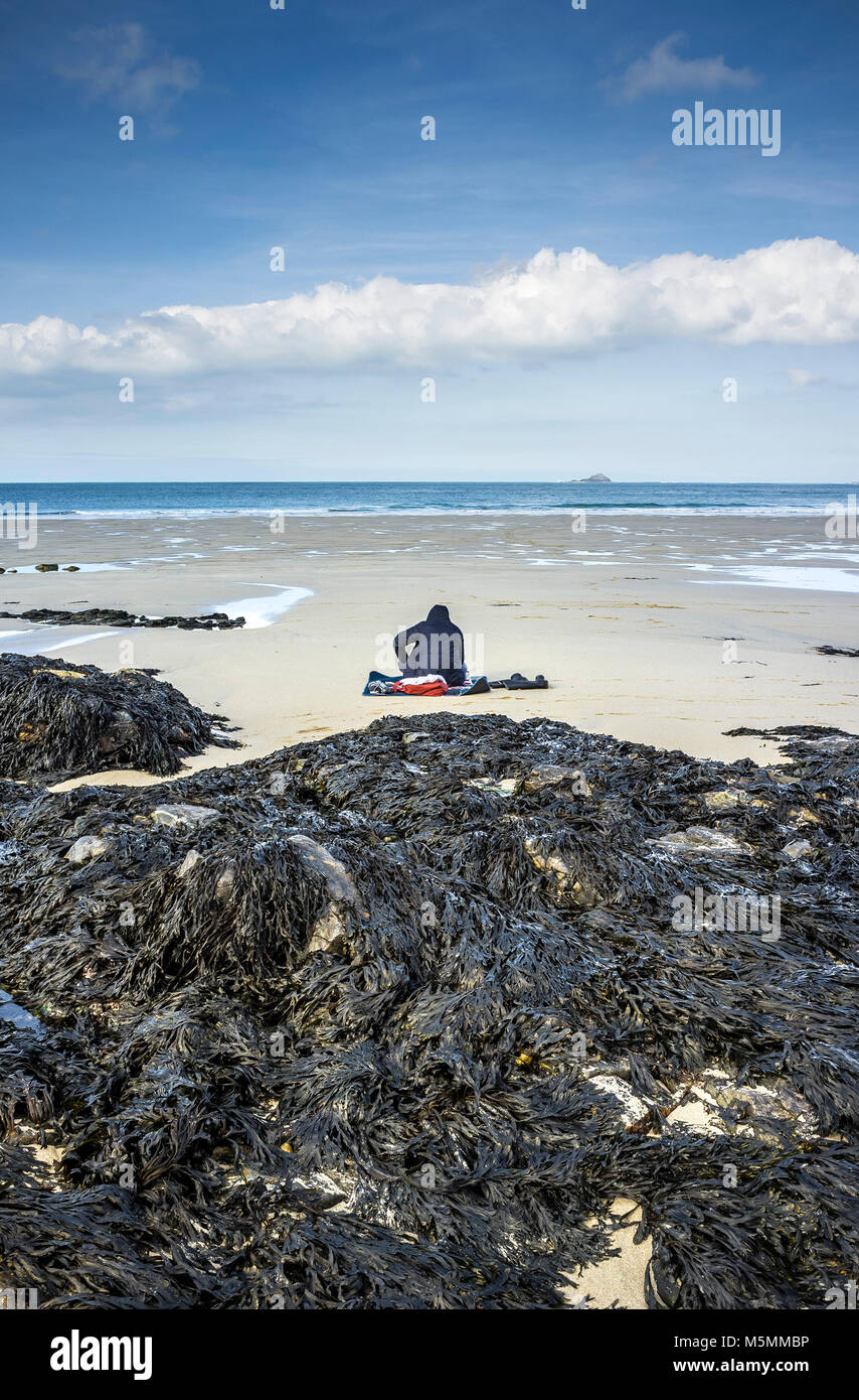 Eine geheimnisvolle Gestalt sitzen am Strand von Sennen Cove in Cornwall. Stockfoto