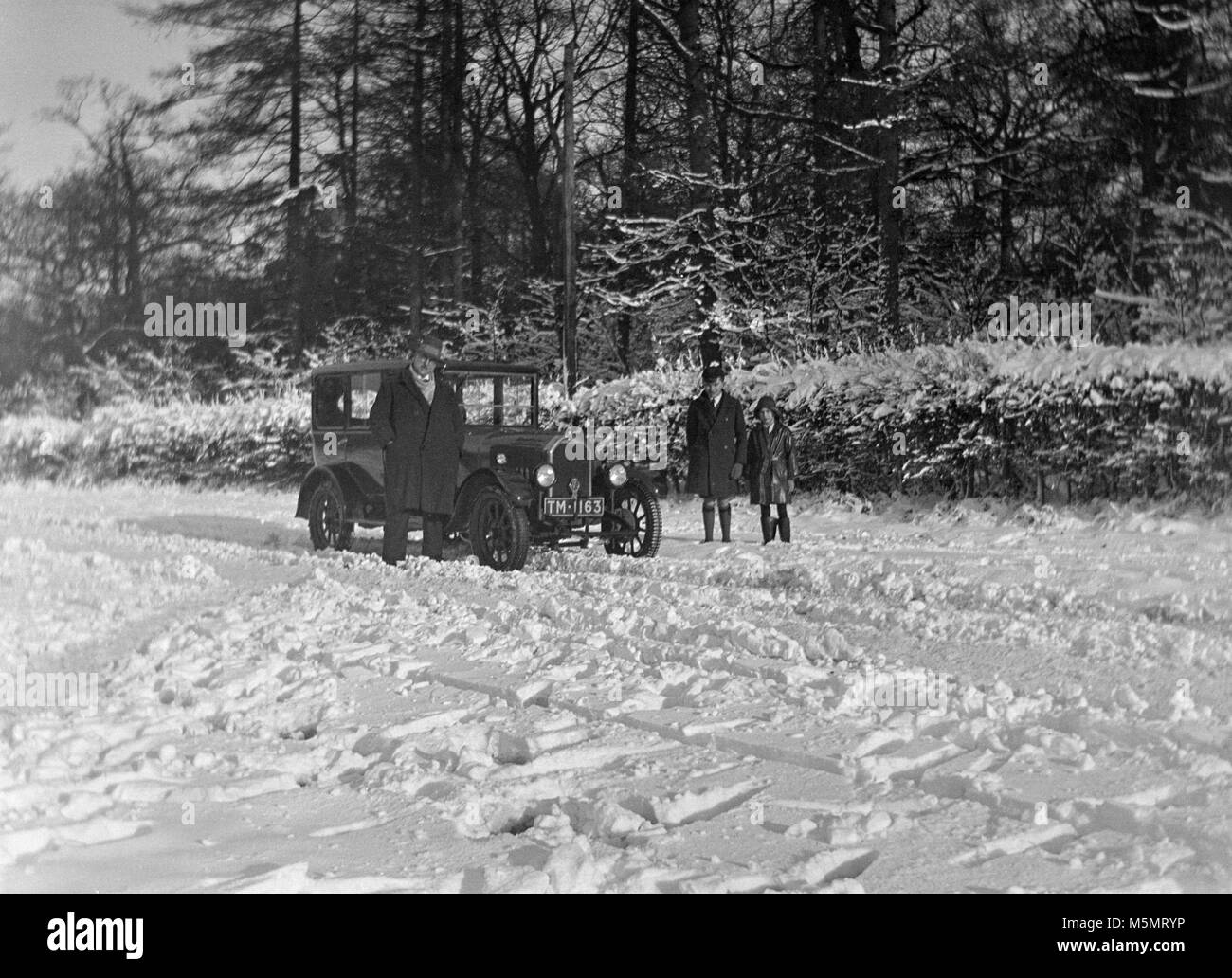 1920 phot eines Autos im Schnee mit zwei Männer und ein Junge außerhalb des Autos. Stockfoto
