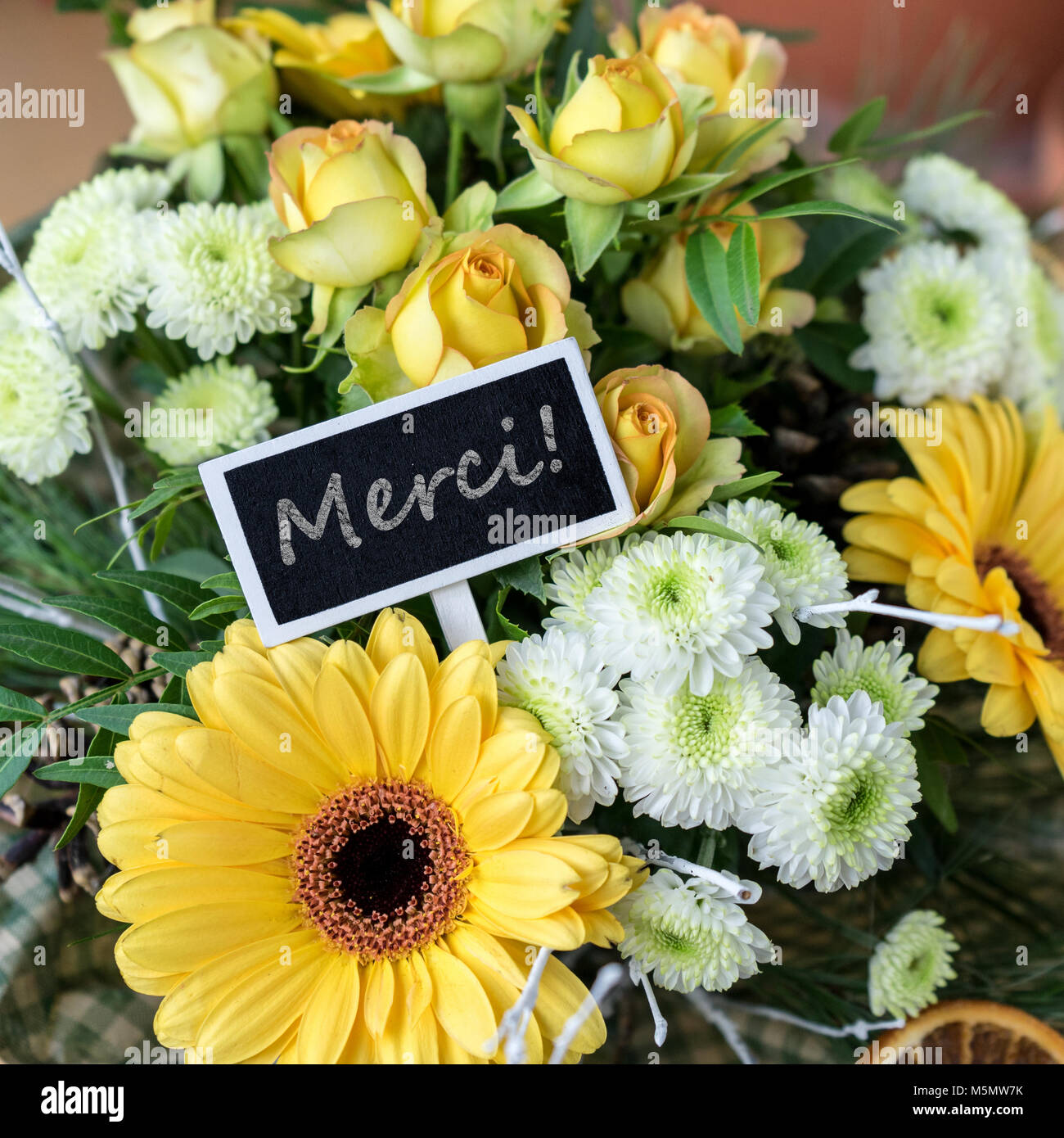 Blumenstrauß aus gelben und weißen Rosen, Gerberas, Chrysanthmen und kleinem Kelch mit französischem Text: Vielen Dank Stockfoto