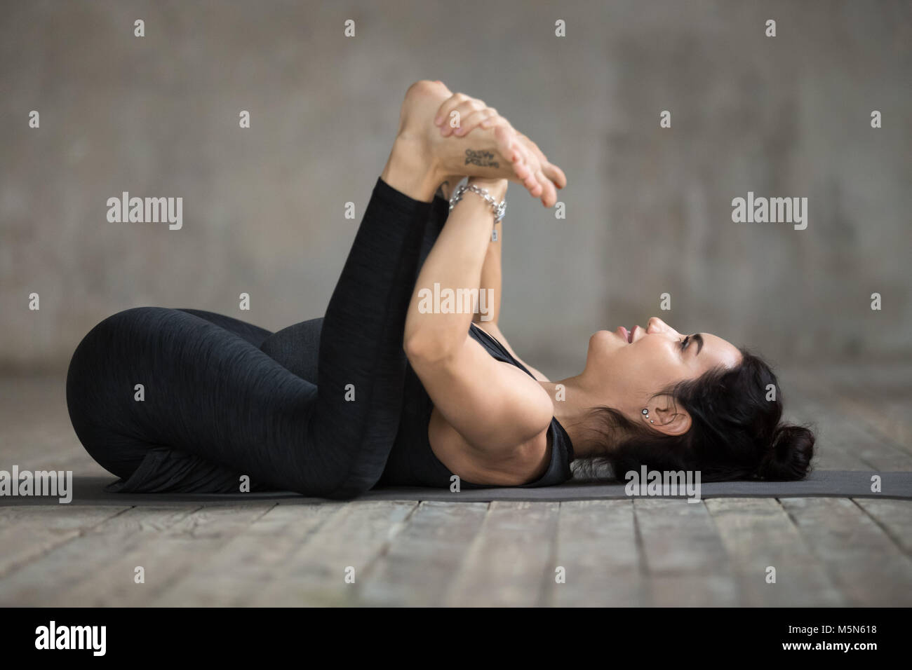 Junge sportliche Frau Üben Yoga, Happy Baby übung, Ananda Balasana darstellen, arbeiten, tragen Sportswear, schwarze Hose und Top, innen voll Stockfoto