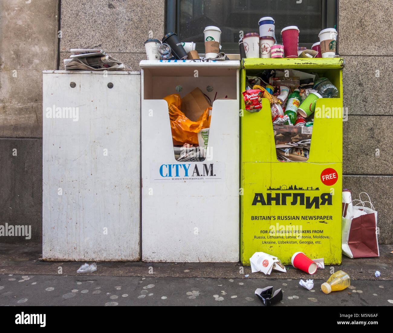 Kostenlose Zeitung steht, verwandelte sich in überquellenden Mülleimer, mit Einstreu, bestehend aus hauptsächlich Getränke Behälter, rund herum. London, England, UK. Stockfoto