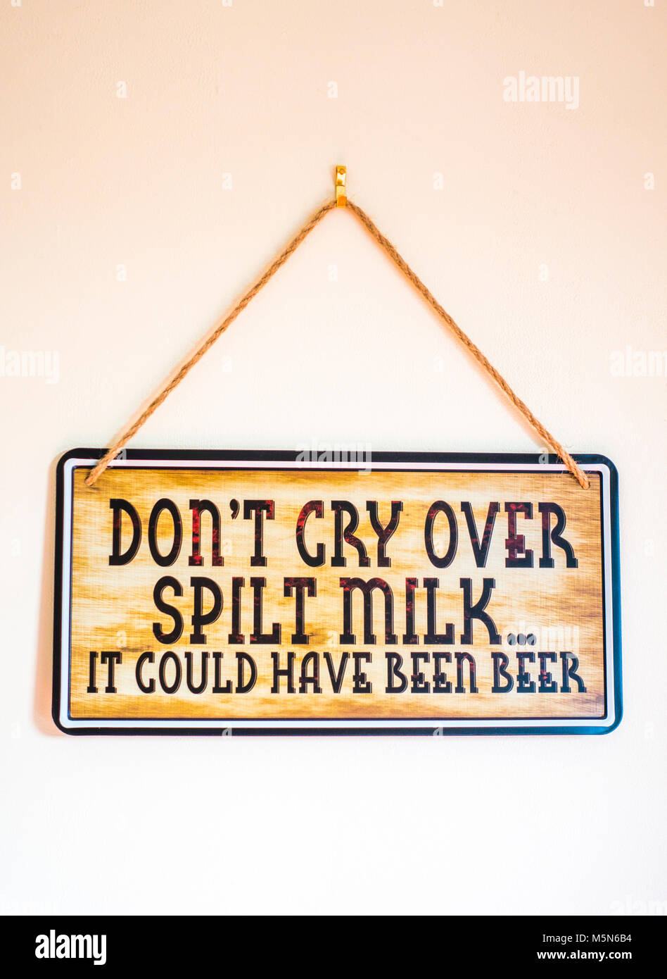Zeichen hängen durch Zeichenfolge an einer Innenwand, die mit dem witzigen Slogan: "Nicht über verschüttete Milch weinen... Es könnte Bier wurden". England, UK. Stockfoto