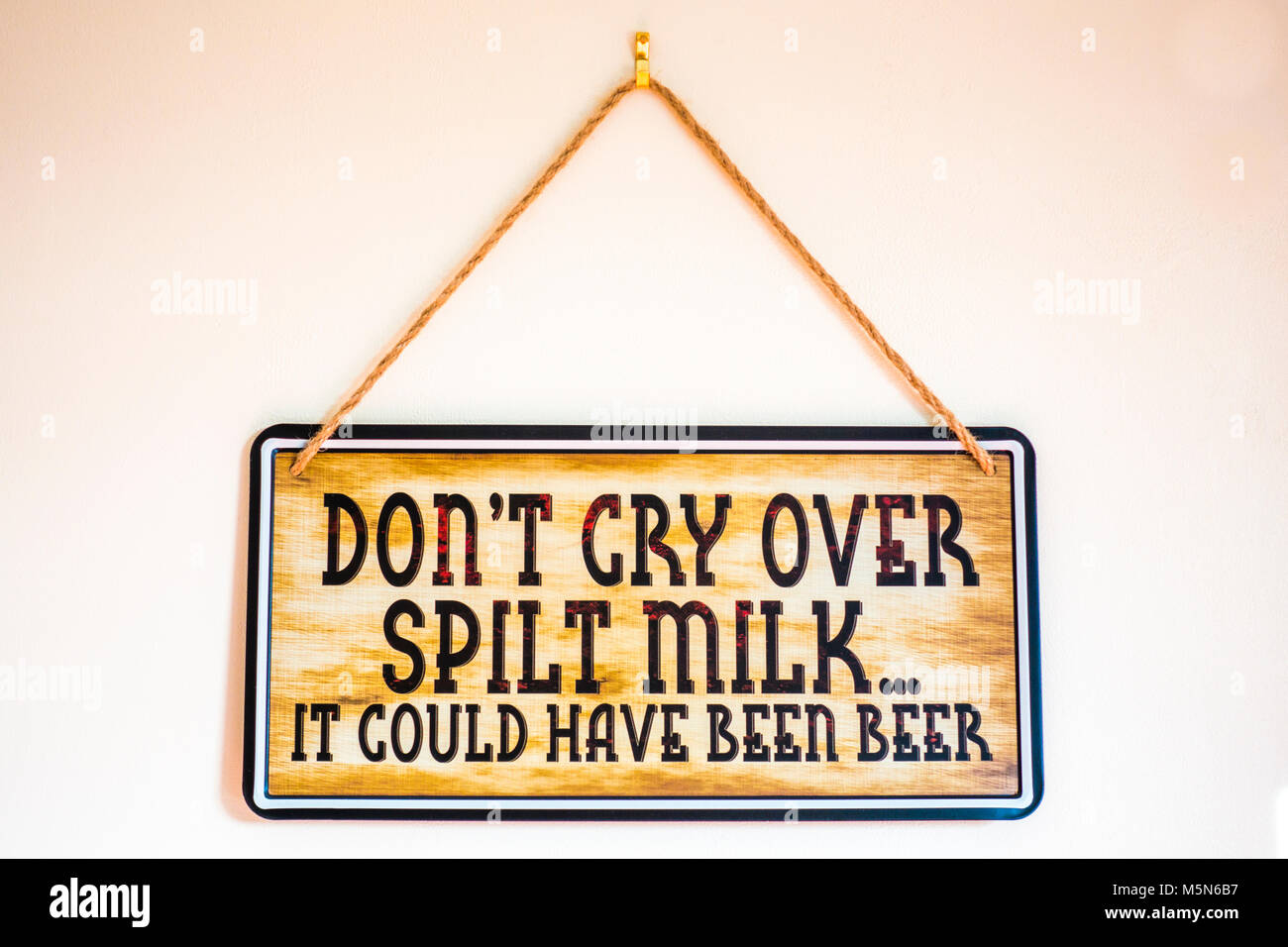 Zeichen hängen durch Zeichenfolge an einer Innenwand, die mit dem witzigen Slogan: "Nicht über verschüttete Milch weinen... Es könnte Bier wurden". England, UK. Stockfoto