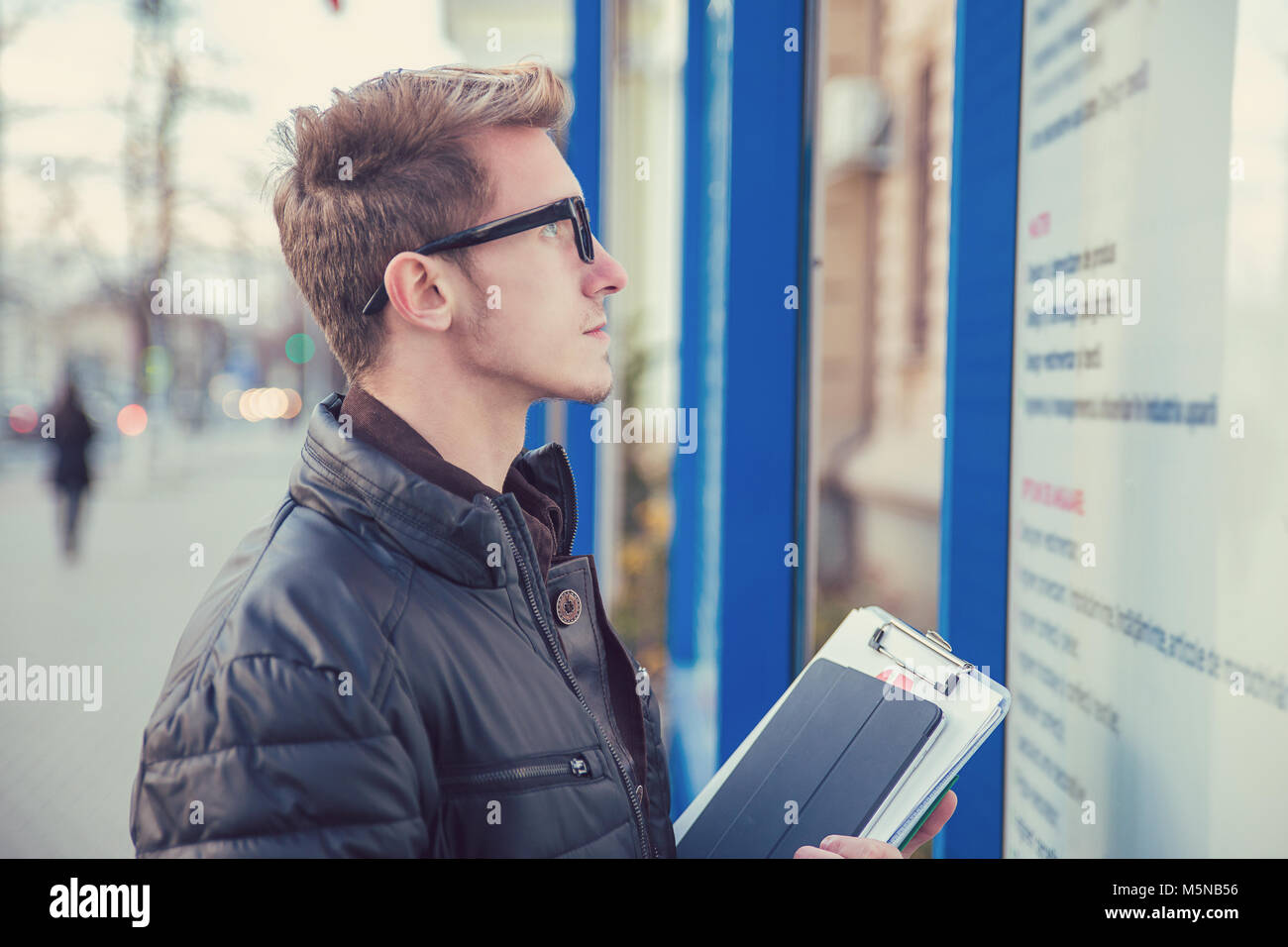 Seitenansicht des stattlichen Student in Gläser holding Dokument und Pad auf Informationen vor. Stockfoto