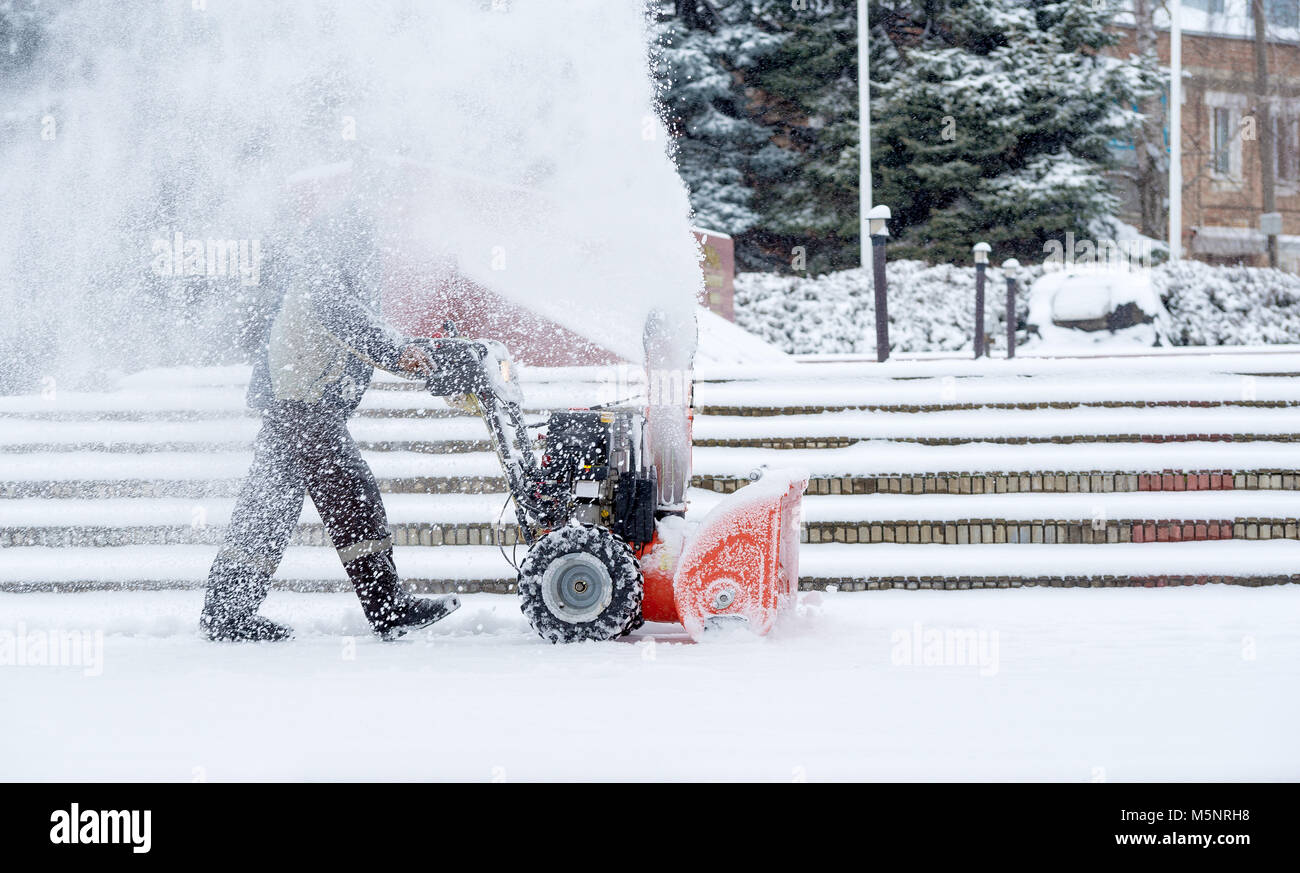 Schnee - Ausbau der Arbeit mit einer Schneefräse. Mann aus Schnee. von Starkniederschlägen und Schnee Stapel Stockfoto