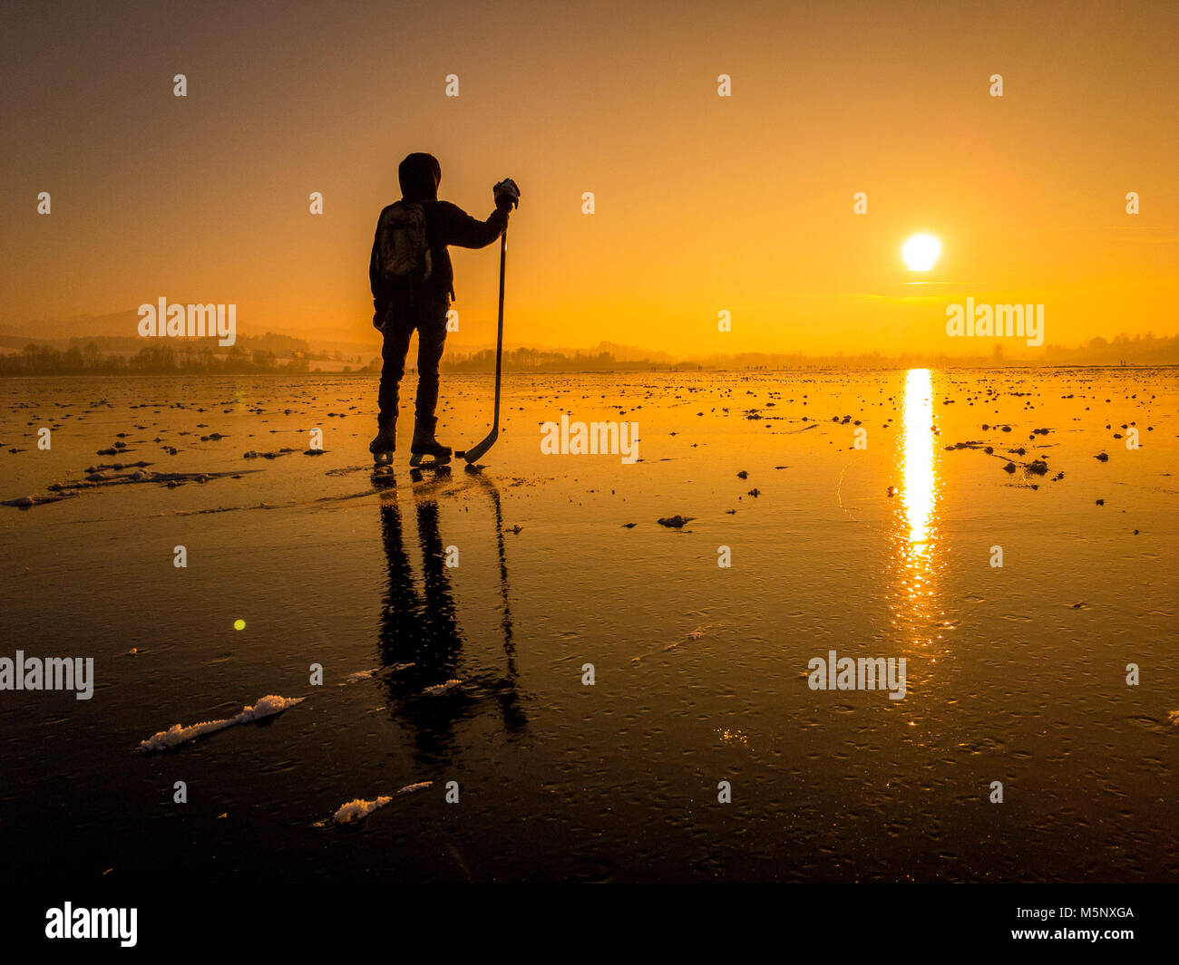 Einen herrlichen Blick auf die Silhouette eines jungen Hockeyspieler stehend auf einem zugefrorenen See mit erstaunlichen Überlegungen im schönen goldenen Abendlicht Stockfoto