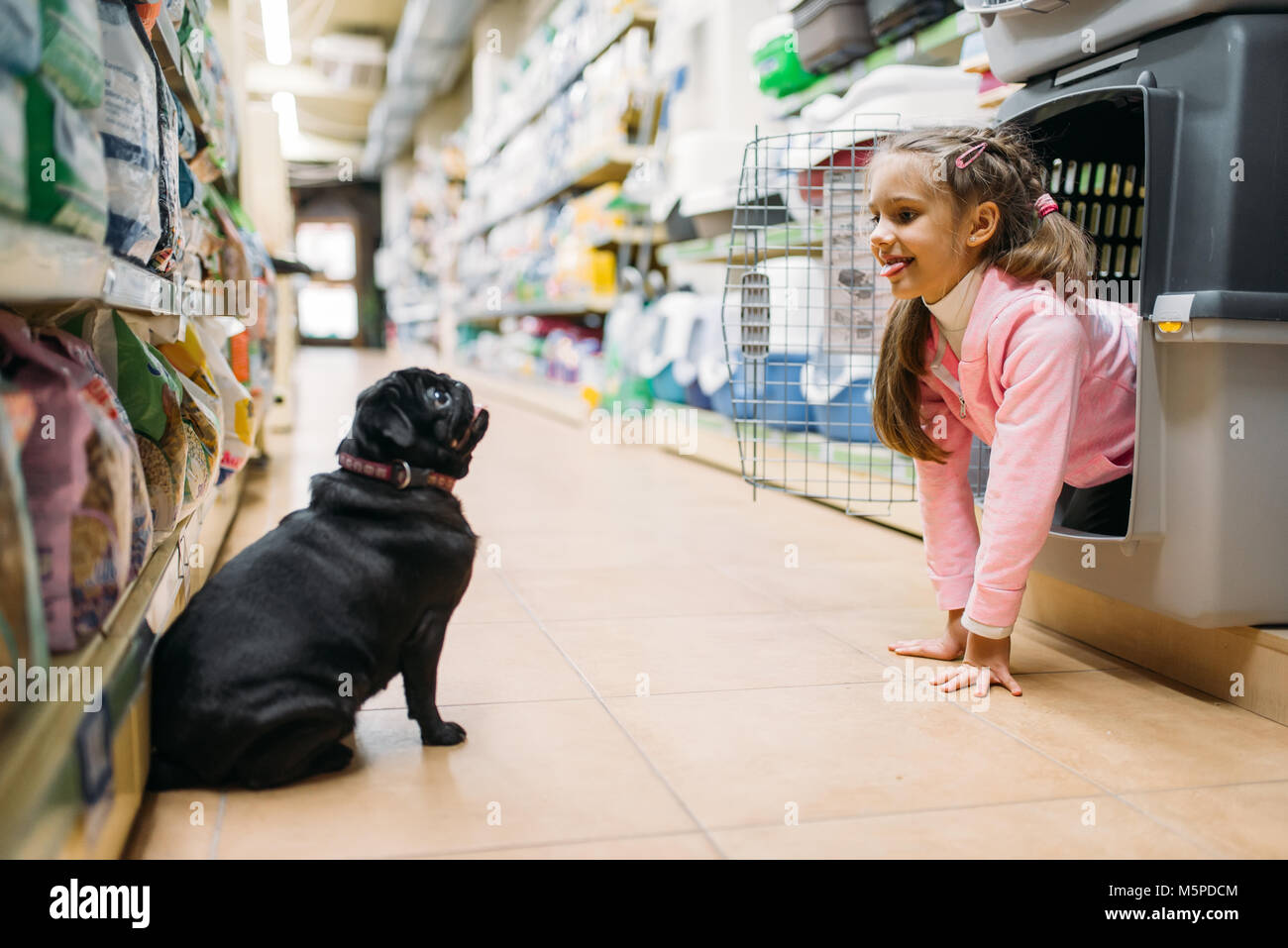 Kleines Mädchen spielt mit den Welpen in Pet Shop, Freundschaft. Kind mit Hund wählt Träger in petshop, Pflege für Haustiere Stockfoto