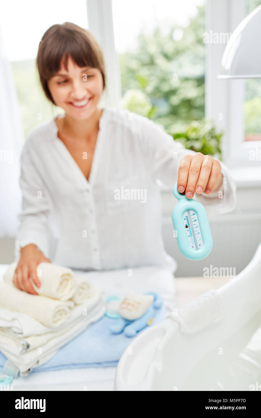 Junge Frau als Mutter hält ein Badethermometer für das Baby Badewanne Stockfoto