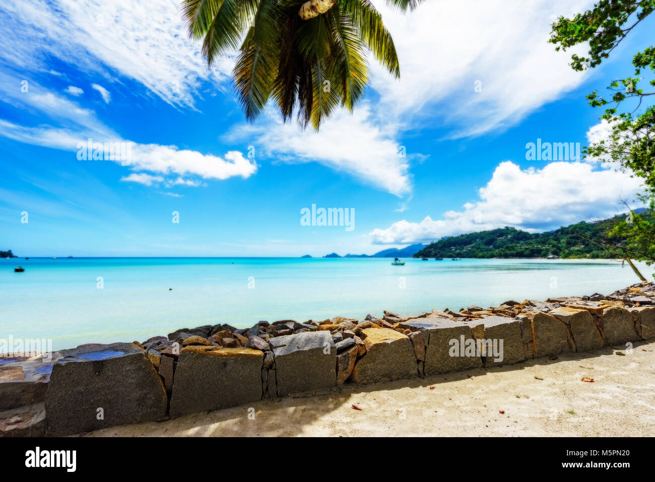 Erstaunlich schöne Lagune mit Booten in türkisfarbenem Wasser hinter Palmenblättern, Seychellen Stockfoto