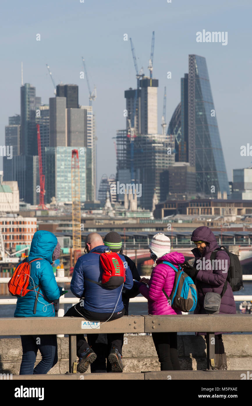 Touristen gekleidet im Winter Kleidung in einer kalten, klaren Tag, stoppen Sie den Blick von der Waterloo Bridge über den Wolkenkratzern der Stadt London, UK zu bewundern. Stockfoto