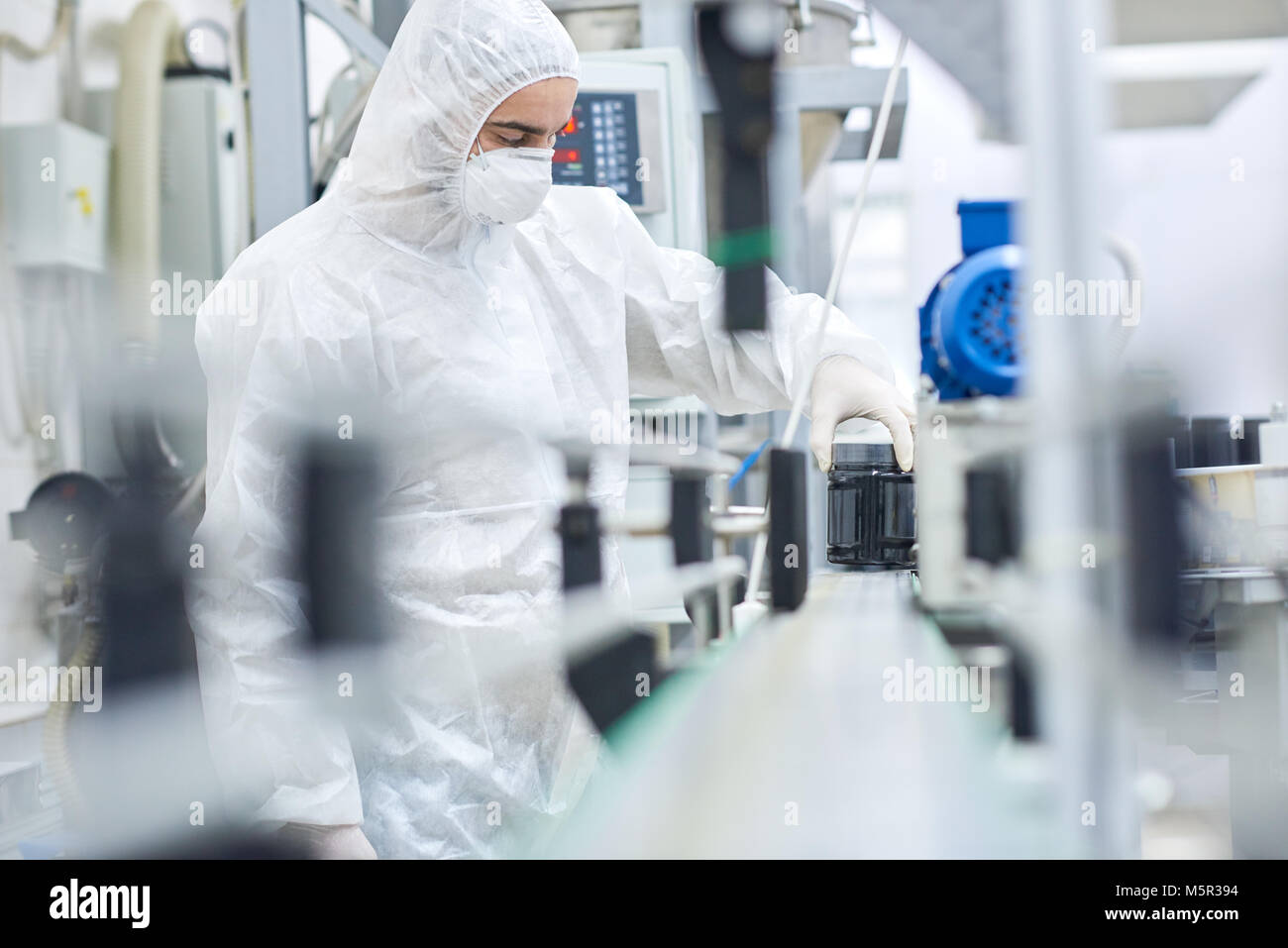 Junger Mann mit Overall und Sicherheit Maske arbeiten auf der Linie der modernen pharmazeutischen Fabrik, Portraitfotos Stockfoto