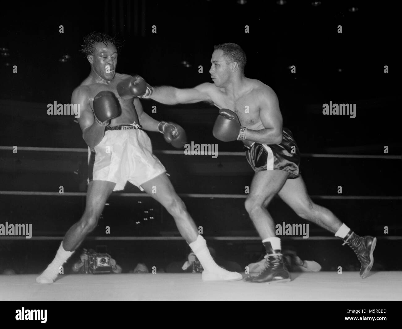 Kid Gavilan nimmt einen Durchschlag von Walter Byars bei einem Boxkampf in Chicago im Jahr 1957. Gavilan, aus Kuba, war ein welterweight World Champion. Stockfoto