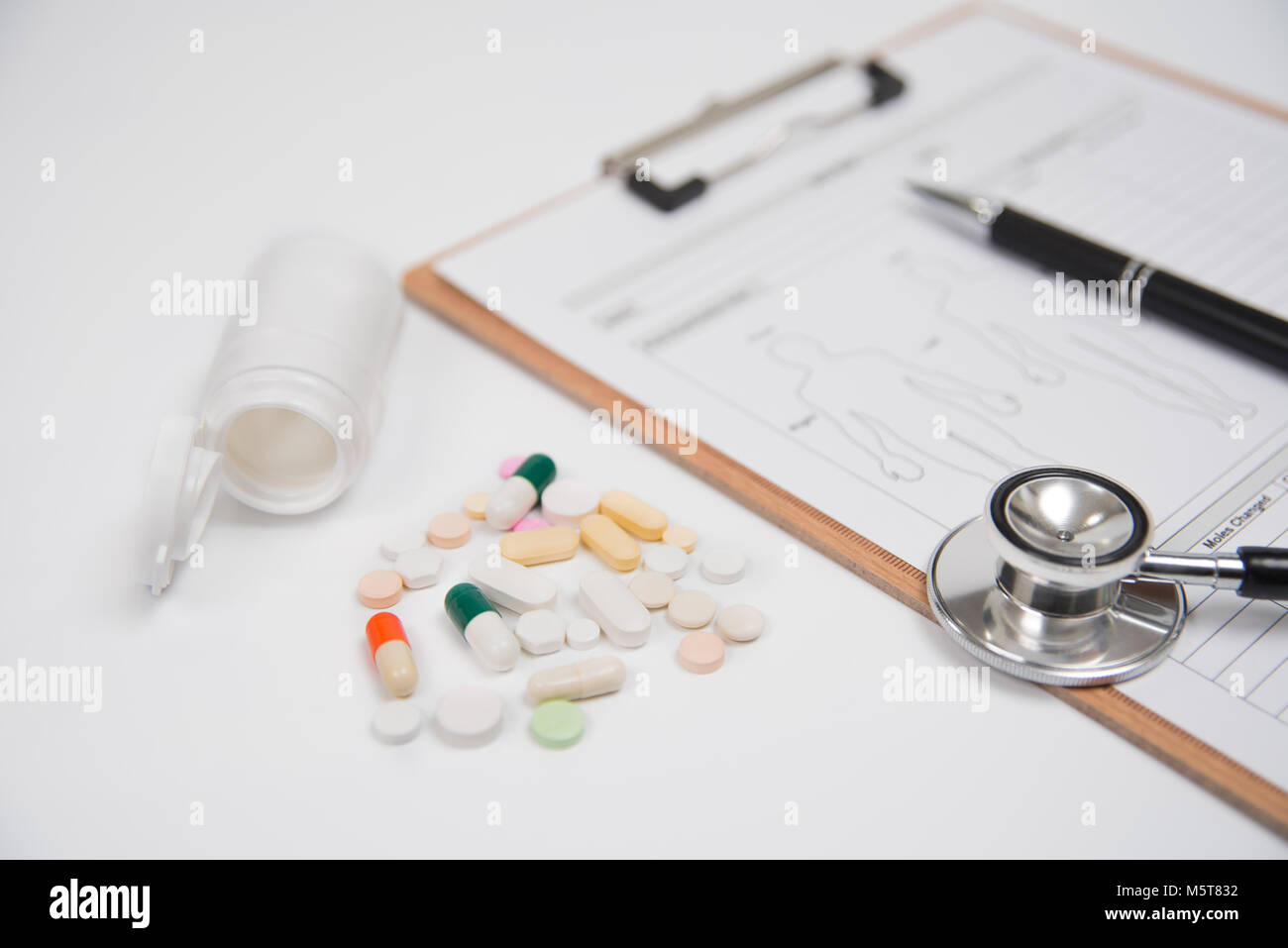 Pillen und eine weiße Flasche, zusammen mit einem Stethoskop und ein medizinisches Diagramm, werden über einen weißen Hintergrund. Für Gesundheit und medizinische Industrie verwendet Stockfoto