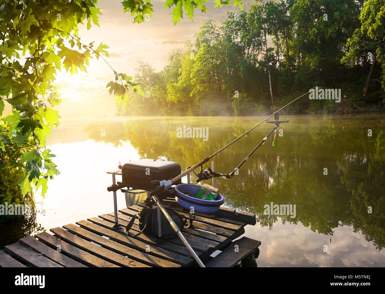 Angelausrüstung auf hölzernen Pier und ruhigen Fluss am Morgen Stockfoto