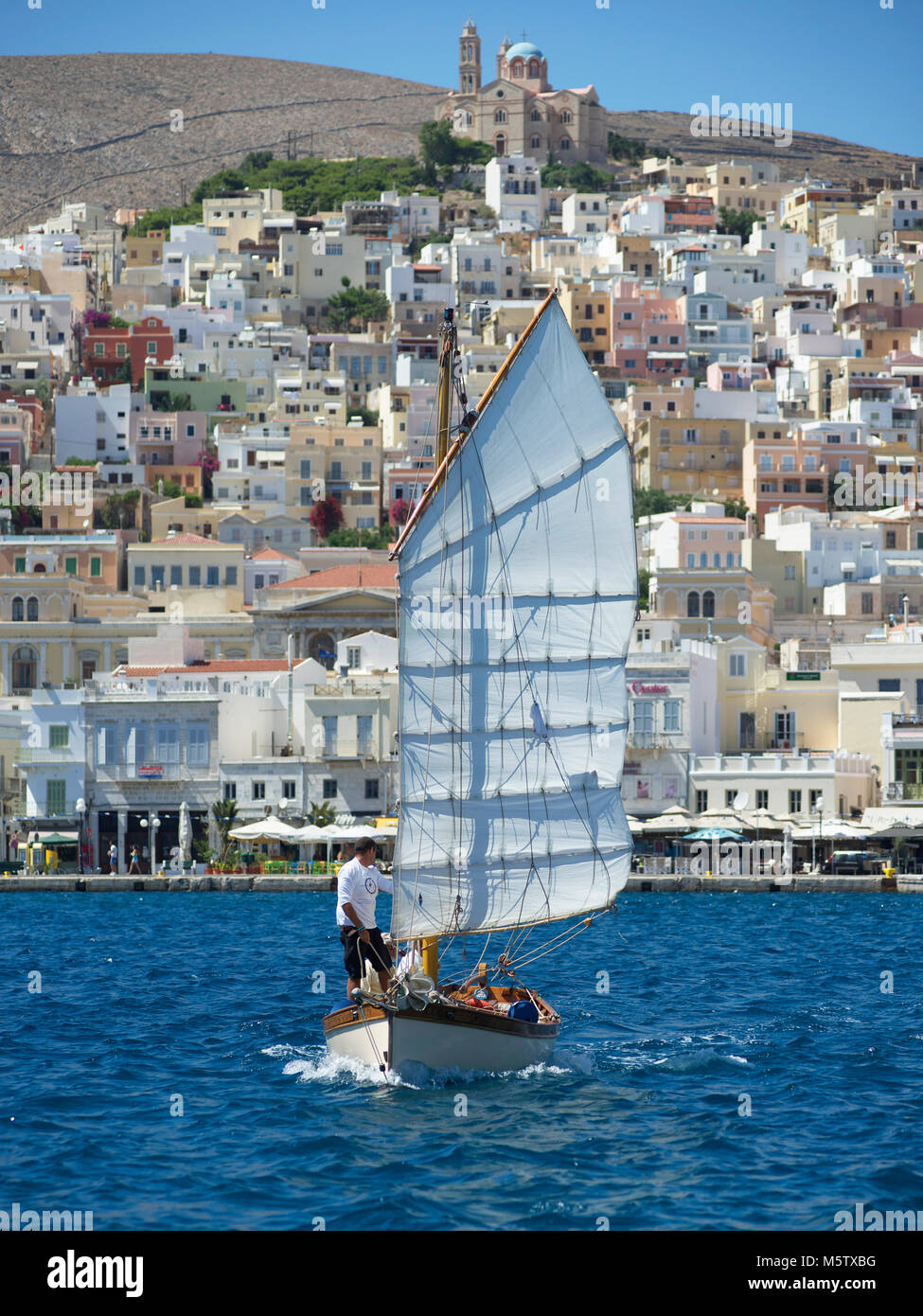 Das Segelboot Chryssopigi Segel aus Syros Hafen, in Griechenland. Die griechisch-orthodoxe Kirche der Auferstehung Christi sichtbar ist. Stockfoto