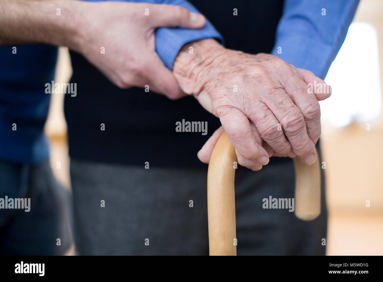 Der ältere Mann die Hände auf Gehstock mit Sorgfalt Arbeiter im Hintergrund Stockfoto