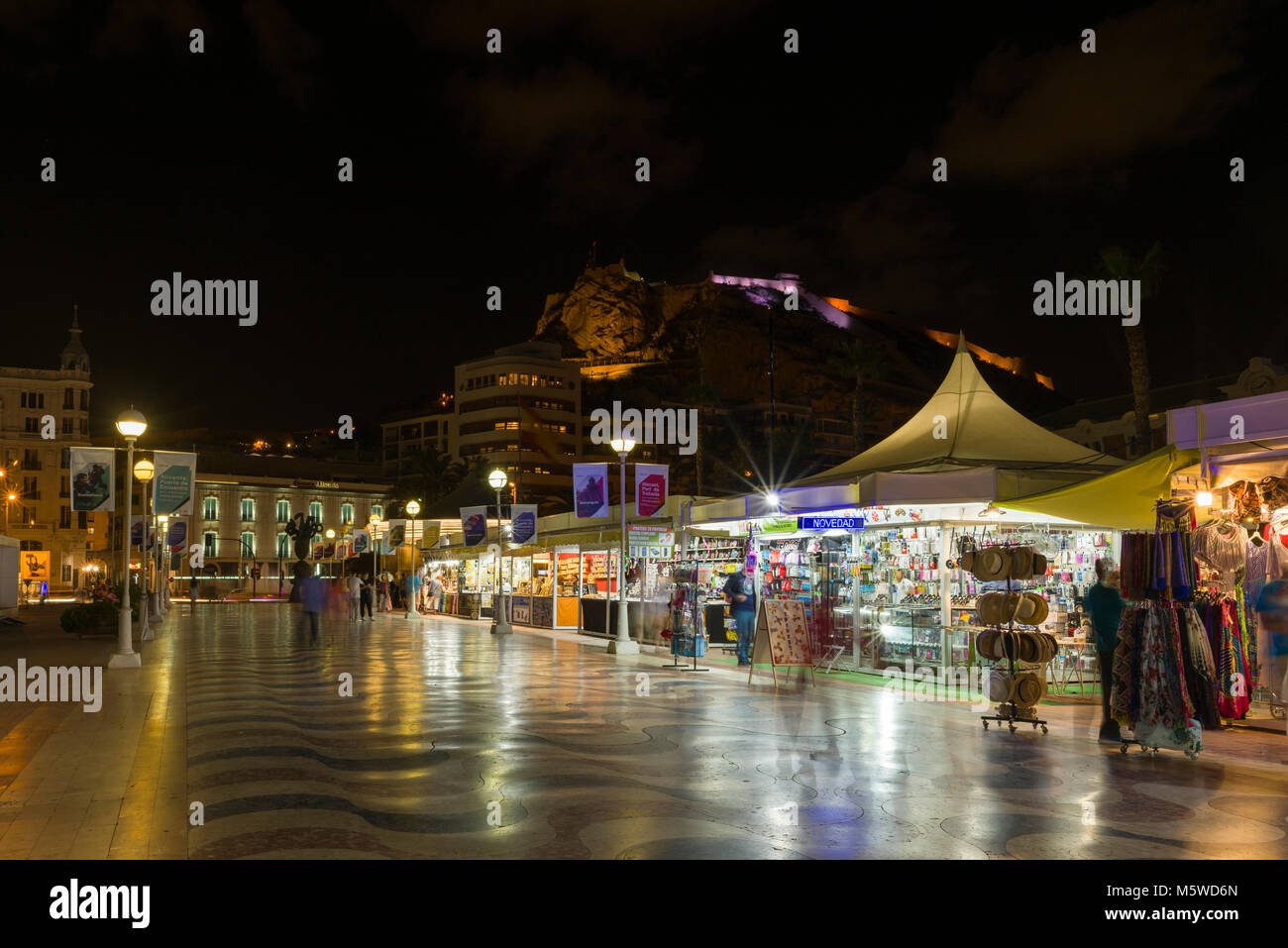 Marktstände entlang der Hafenpromenade in der Nacht mit der Burg Santa Barbara über, Alicante, Spanien. Stockfoto