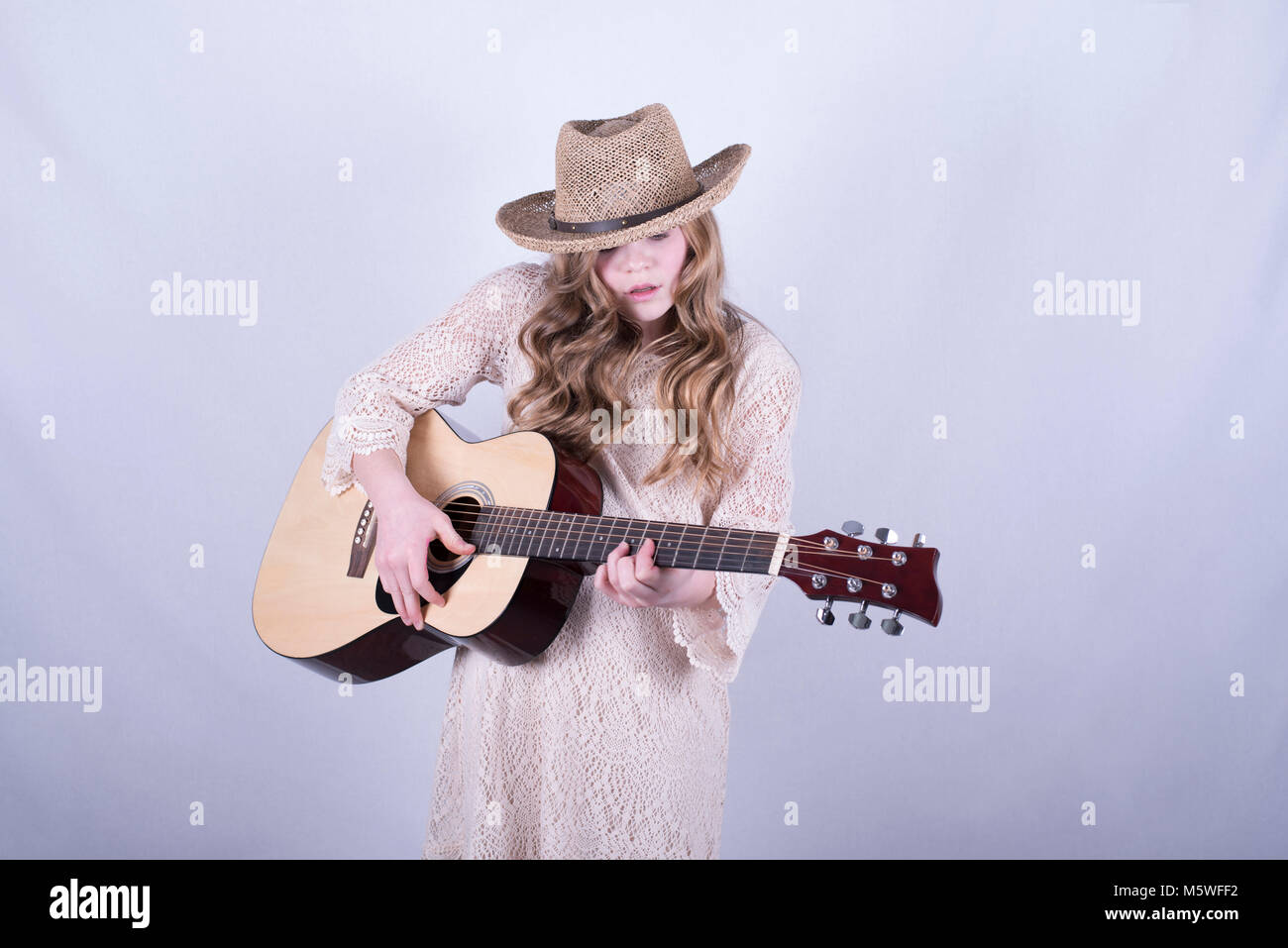 Der 12-jährige Mädchen mit langen, schmutzig blonden Haar und tragen Strohhut spielen Akustische 6-saitige Gitarre vor weißem Hintergrund Stockfoto