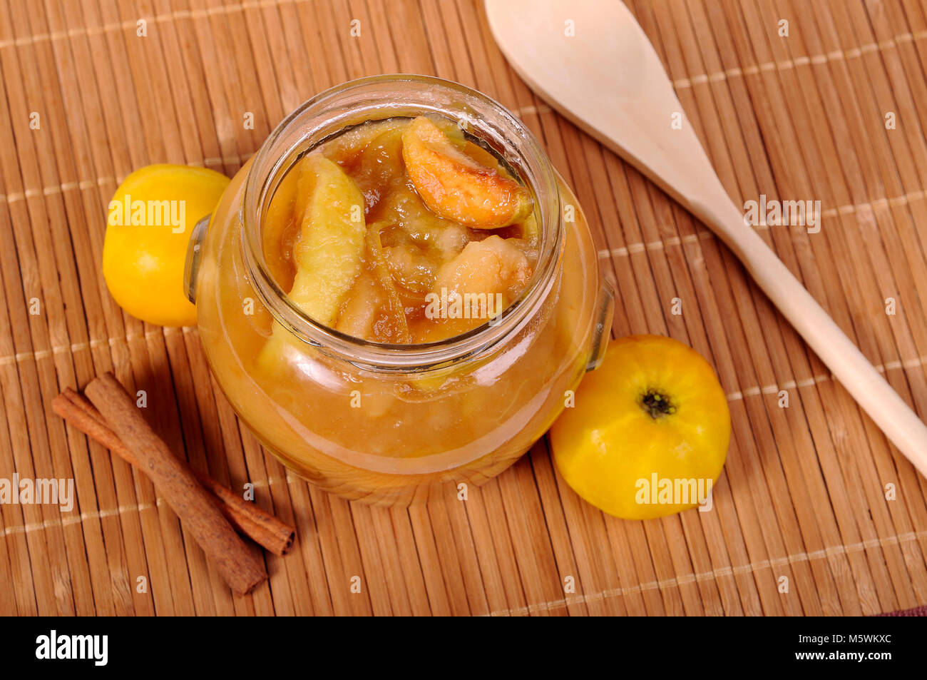 Glas Glas mit Apple Jam, gelbe Äpfel, Zimt und Löffel aus Holz Stockfoto