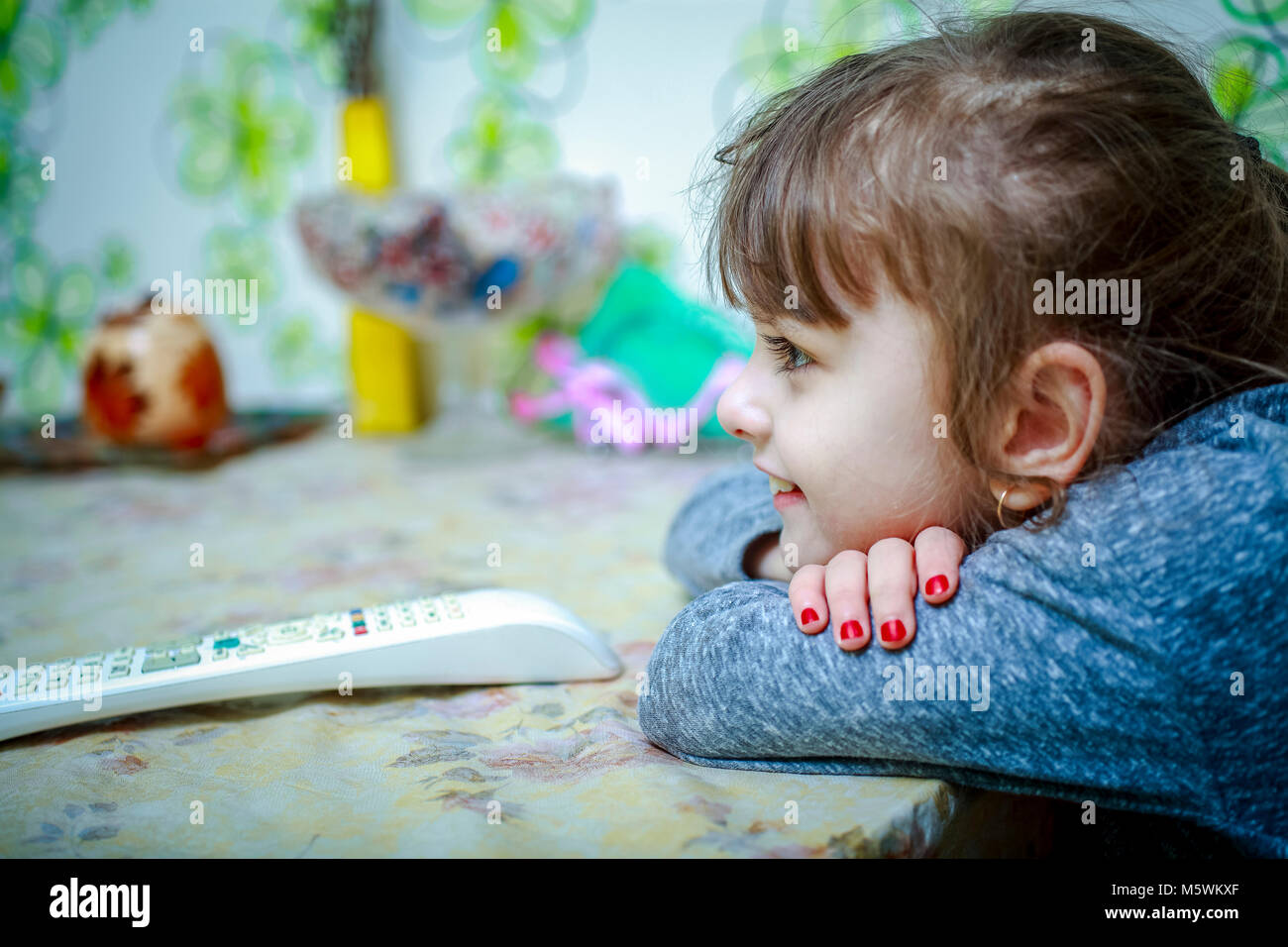 Das Baby sitzt am Tisch, neben der TV-Fernbedienung Stockfoto