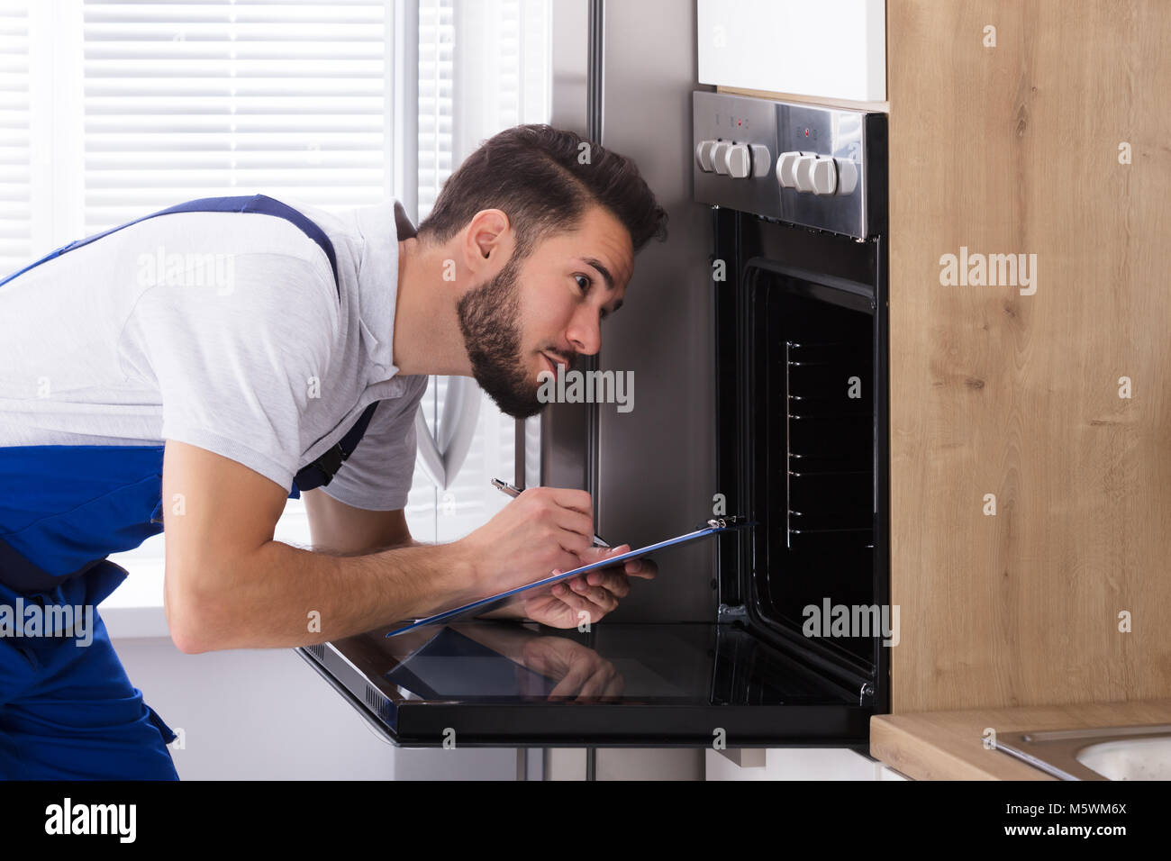 Junge männliche Elektriker Schreiben auf Zwischenablage beim Betrachten Ofen in der Küche Stockfoto