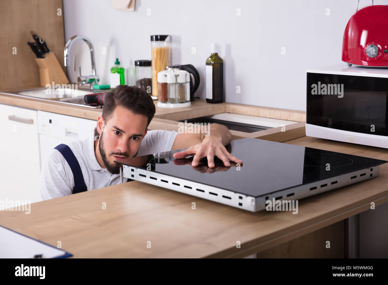 Junge männliche Techniker Prüfung Induktion Herd in der Küche Stockfoto Junge männliche Techniker Prüfung Induktion Herd in der Küche Stockfoto
