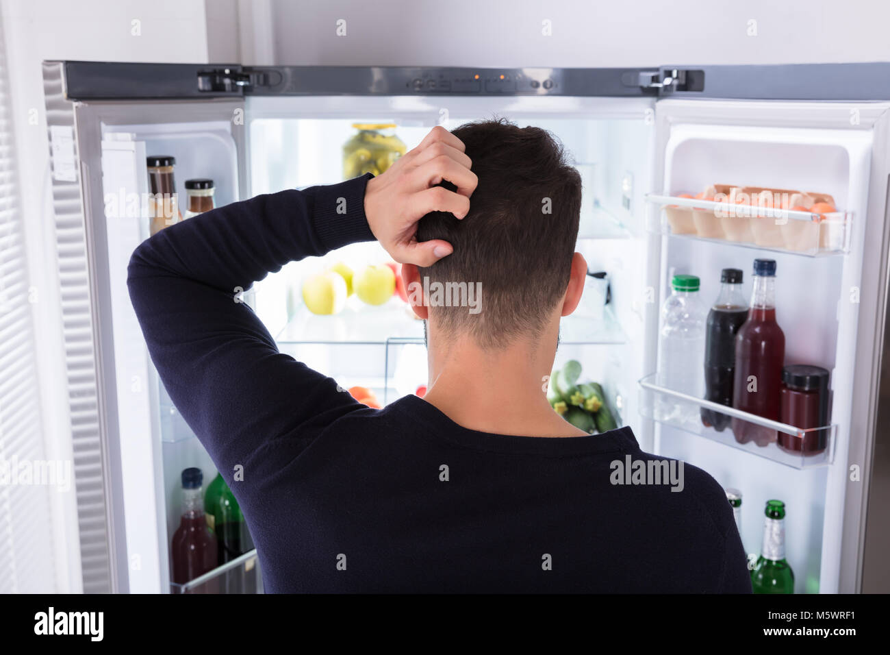 Rückansicht eines verwirrten jungen Mann auf der Suche nach Essen im Kühlschrank Stockfoto