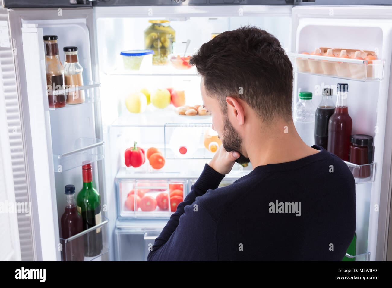 Rückansicht eines verwirrten jungen Mann auf der Suche nach Essen im Kühlschrank Stockfoto