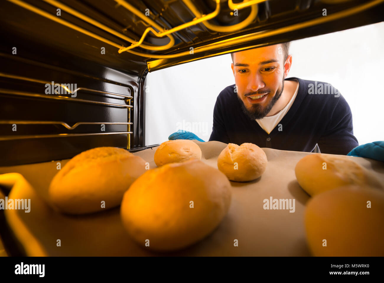 Glückliche junge Mann trägt blaue Handschuhe nehmen Sie Fach der gebackenen Plätzchen aus dem Ofen Stockfoto
