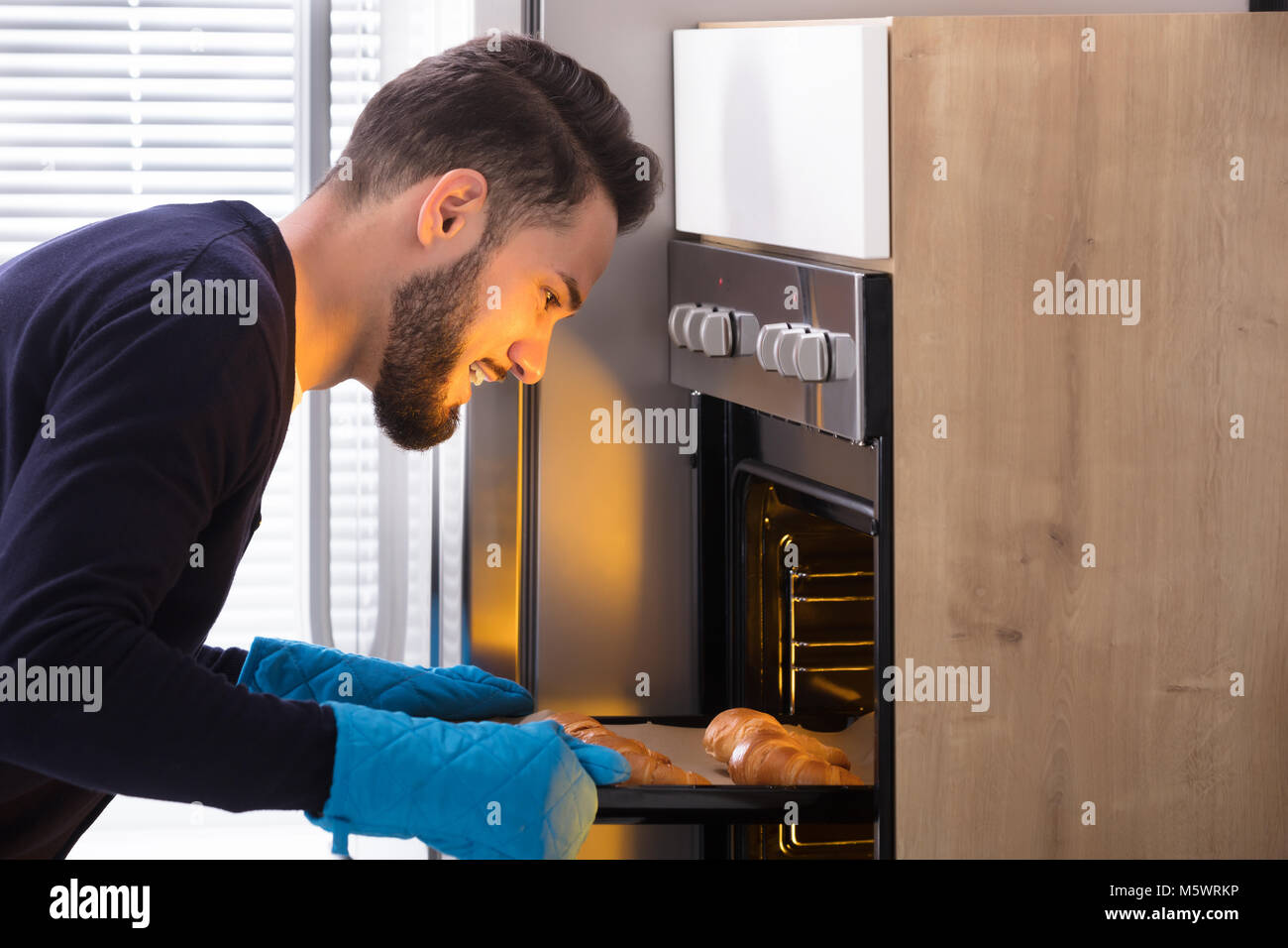 Seitenansicht eines lächelnden jungen Mann nehmen Sie Fach der gebackenen Croissants aus dem Ofen Stockfoto