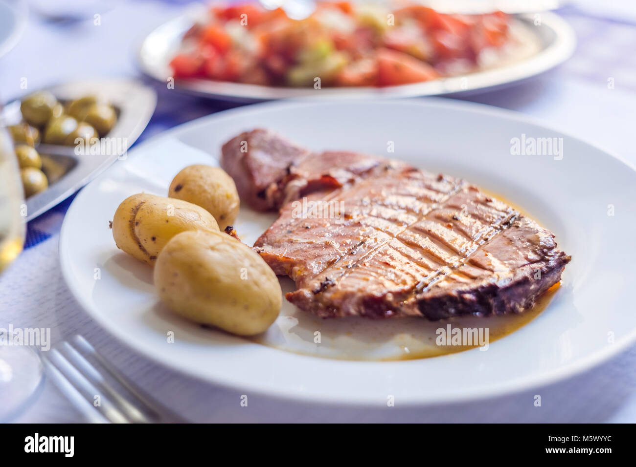 Thunfischsteak mit Kartoffeln, Oliven, Tomaten Salat und Wein auf weiße Platte begleitet Stockfoto