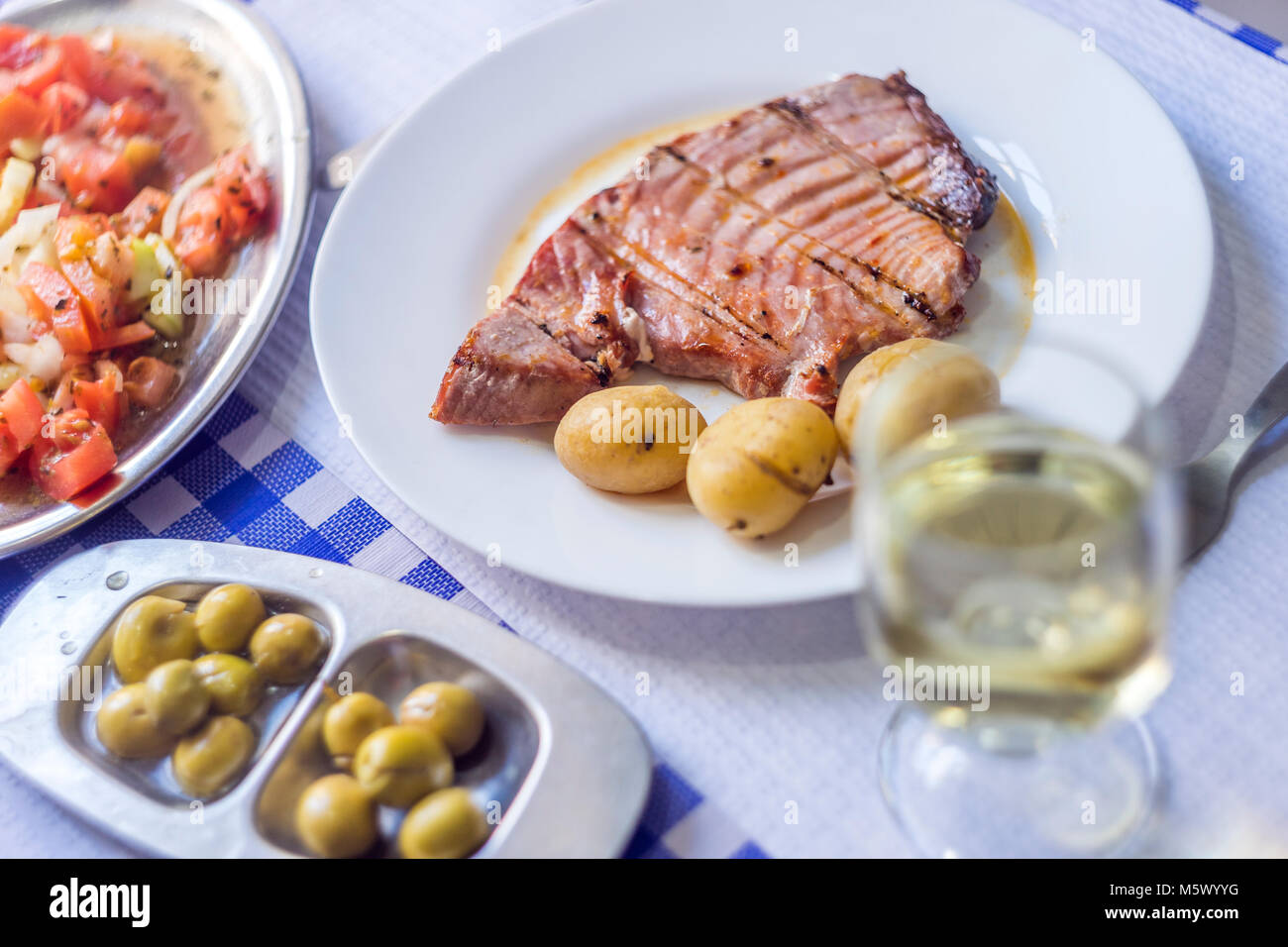 Thunfischsteak mit Kartoffeln, Oliven, Tomaten Salat und Wein auf weiße Platte begleitet Stockfoto