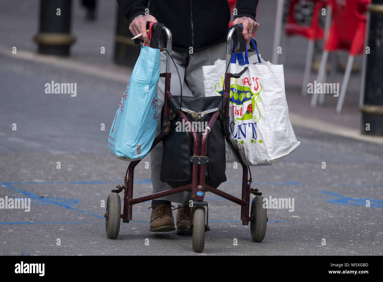 Ein alter Rentner mit einer Gehhilfe für Unterstützung, während auf der Straße tragen Einkaufstaschen in Cardiff, Wales, UK. Stockfoto