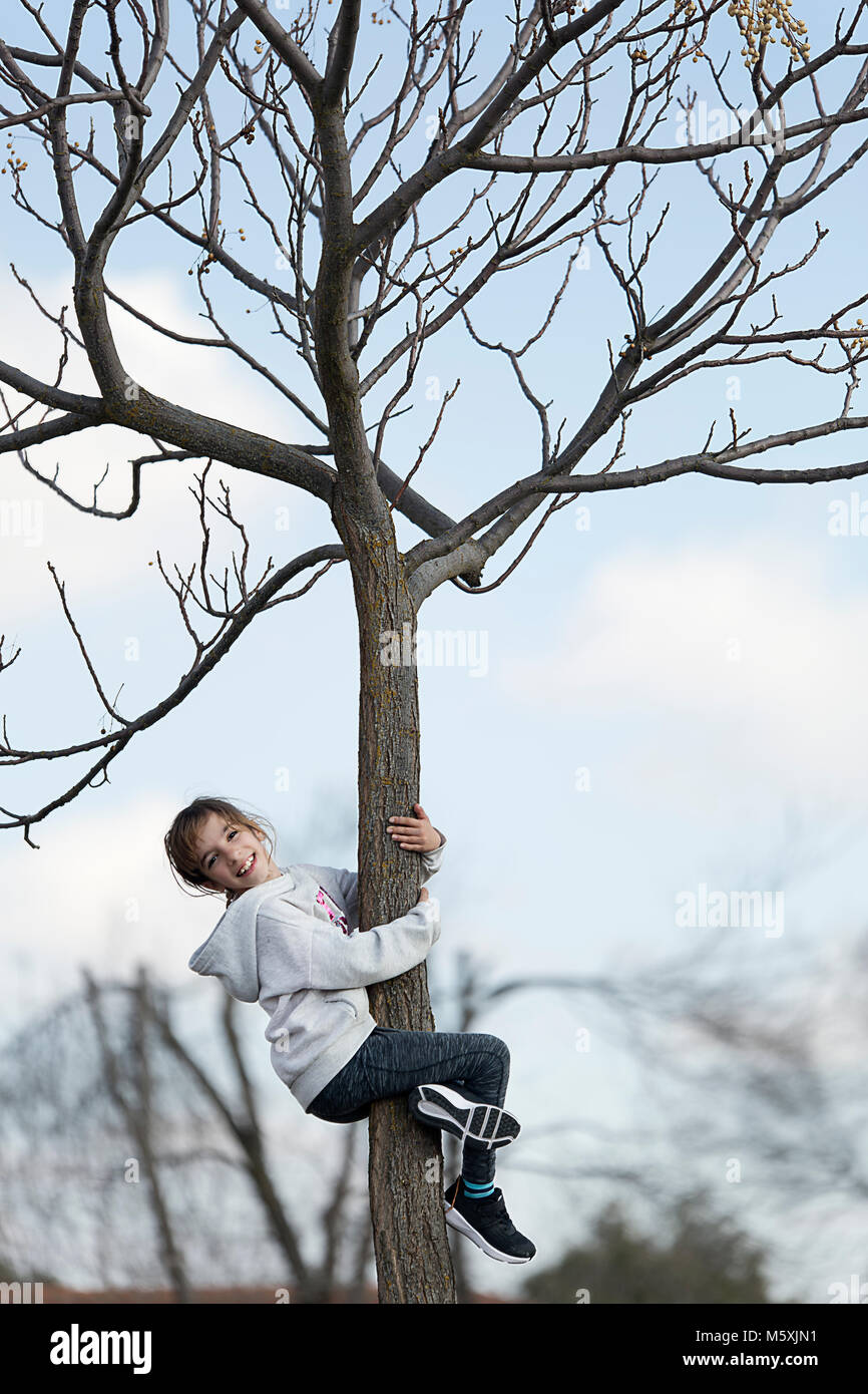 10-jährige Mädchen klettern auf einen Baum in Richtung Kamera schaut. Horizontale shot mit Tageslicht Stockfoto