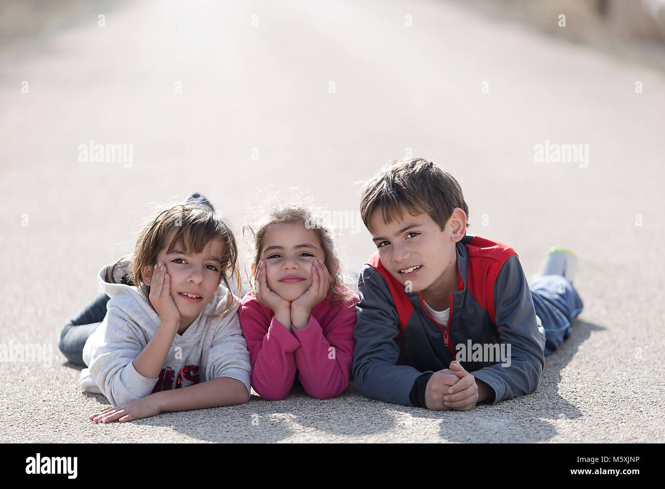Drei Kinder auf dem Boden liegend in einer Straße mit Blick auf die Kamera. Horizontale shot mit Tageslicht Stockfoto