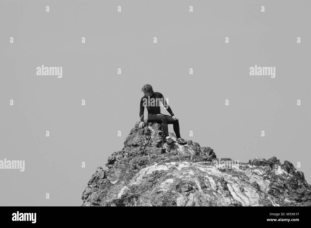 Die Jungen gut aussehenden Surfer, im Neoprenanzug saß auf einem Felsen Stapel auf Holywell Beach, North Cornwall, UK. Englisch am Meer Sommer und Surfen Lifestyle. Stockfoto