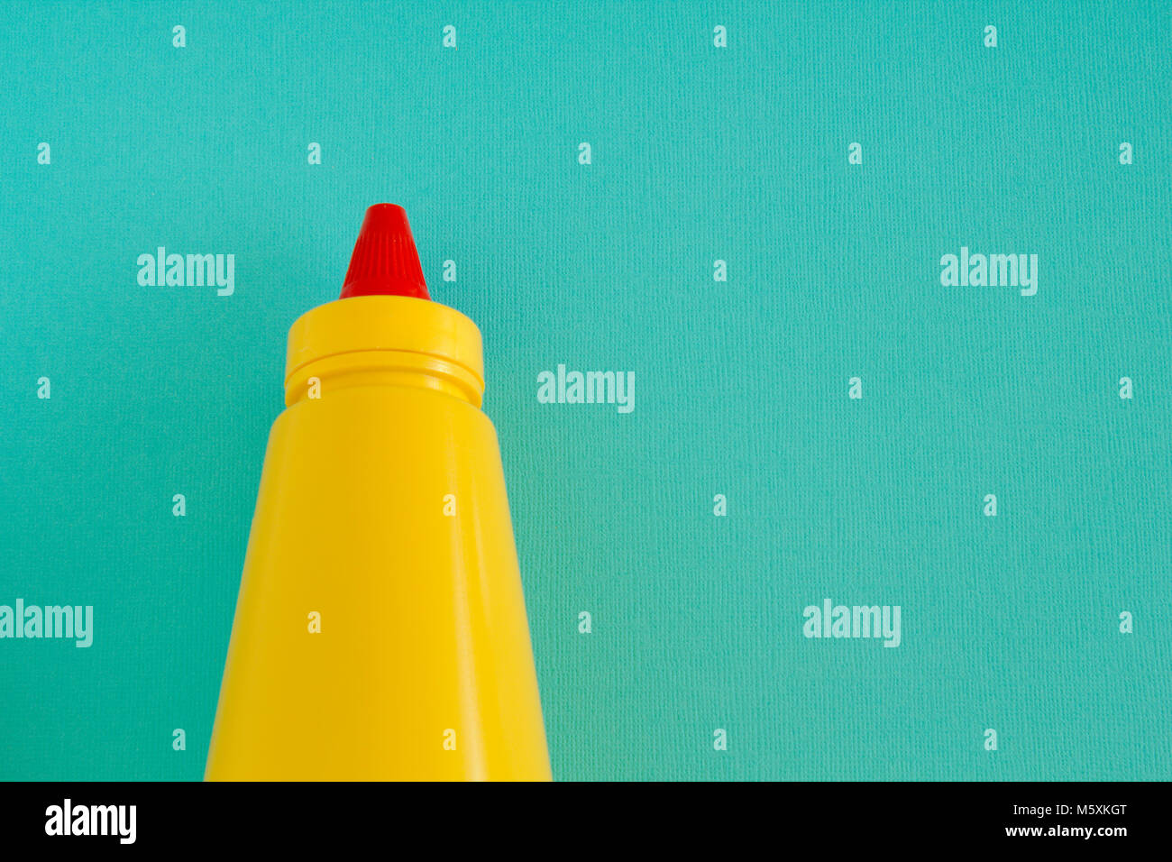 Eine helle gelbe squirting Senf oder Gewürz Flasche mit leuchtend roten verdrehen Deckel. Links auf ein aqua Hintergrund ausgerichtet. Stockfoto