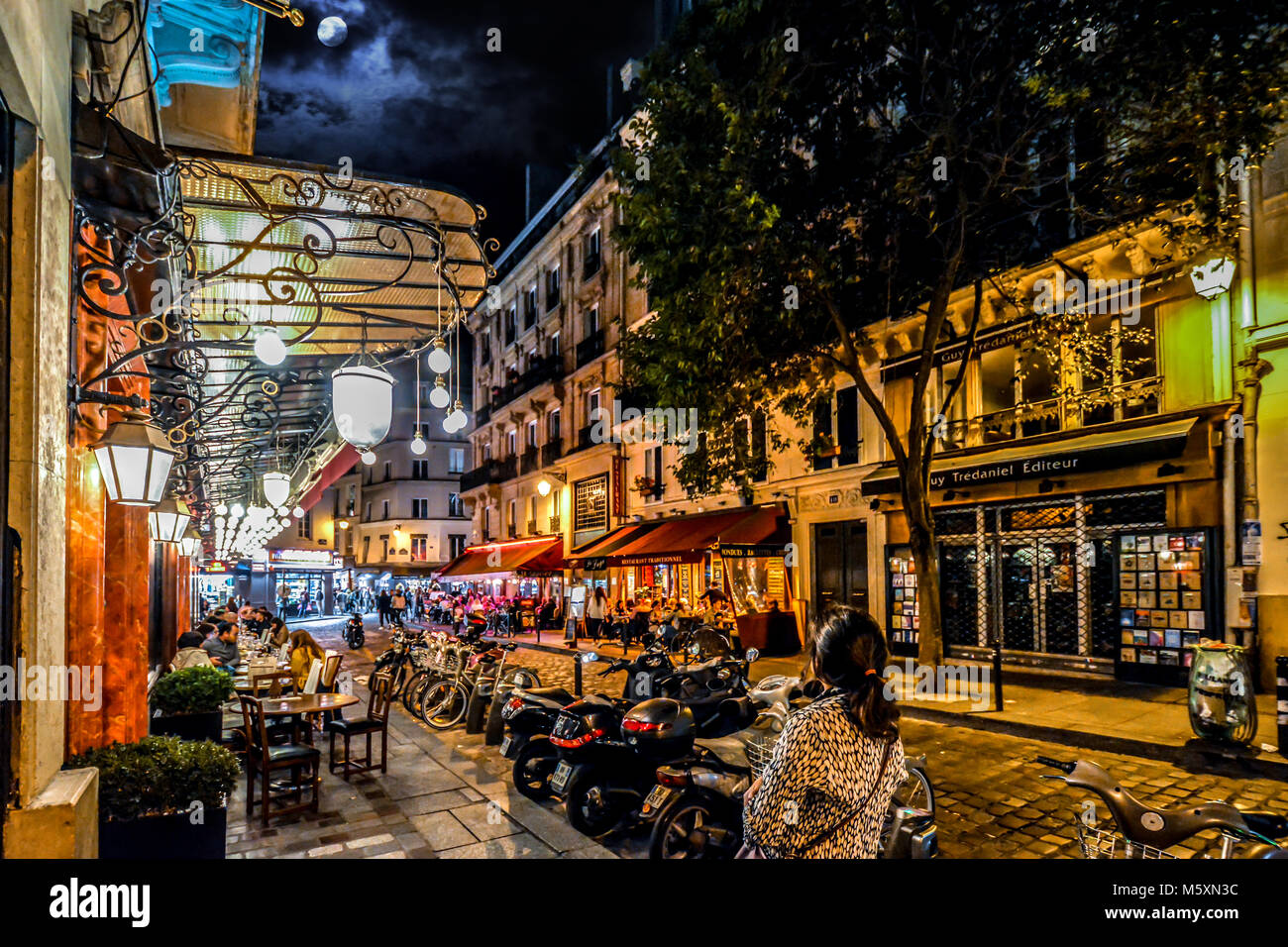 Eine Frau, touristische Wanderungen entlang einer belebten Straße im Quartier Latin von Paris Frankreich mit bunten Cafés, Geschäften und Restaurants bei Vollmond Stockfoto