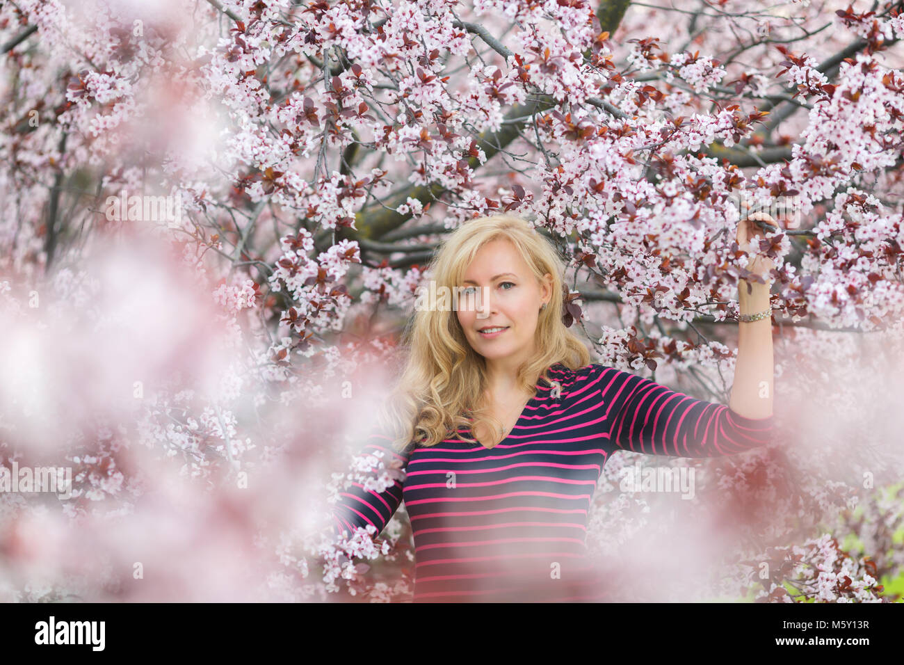 Ein Porträt der kaukasischen Frau mit blonden Haaren in der Nähe von blühenden Kirschbaum, in die Kamera schaut Stockfoto