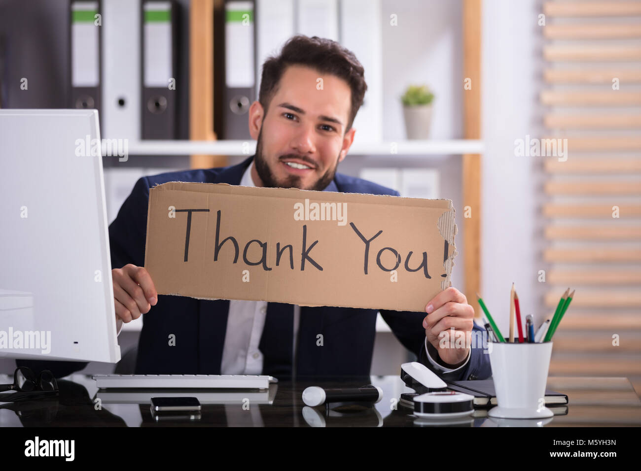 Lächelnde junge Unternehmer Holding Pappe mit vielen Dank Text im Büro Stockfoto