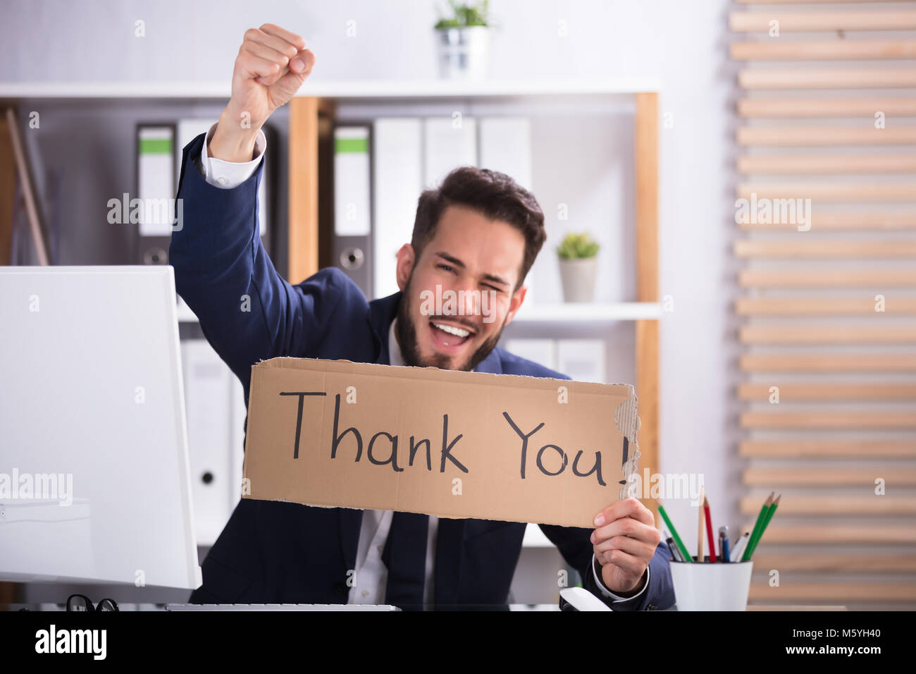 Lächelnde junge Unternehmer hob seine Arme, während Sie Karton mit vielen Dank Text Stockfoto