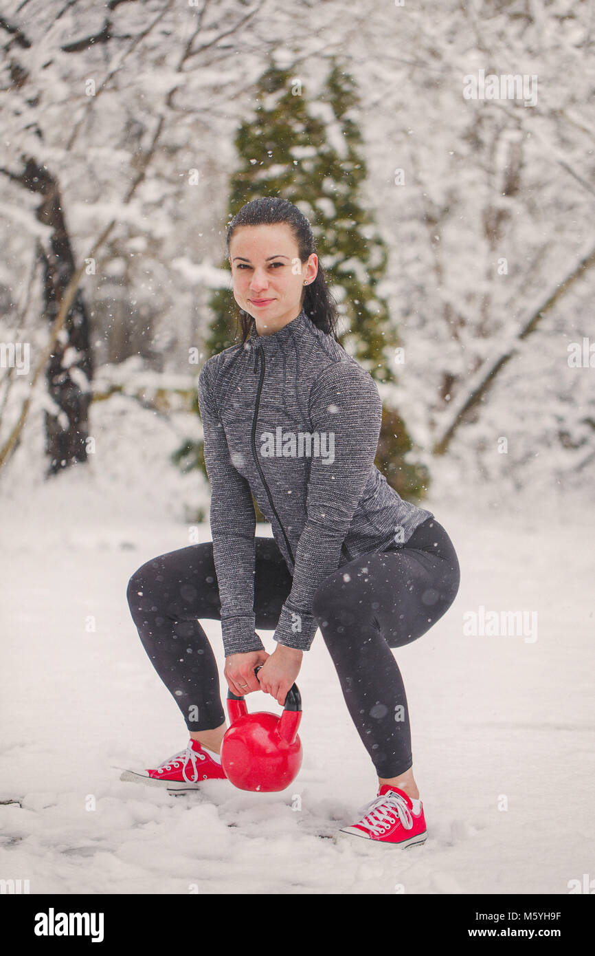 Junge Frau tun Hocke Übung mit den Kettlebells im Schnee im Winter Outdoor Stockfoto