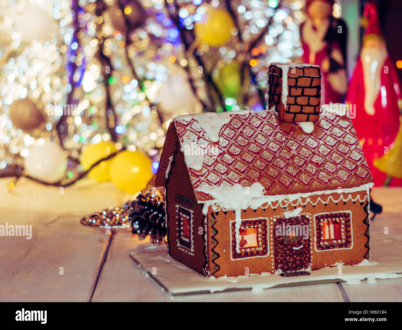 Hausgemachte Weihnachten Lebkuchen Haus auf einem Holztisch. Weihnachtsbeleuchtung im Hintergrund. Stockfoto