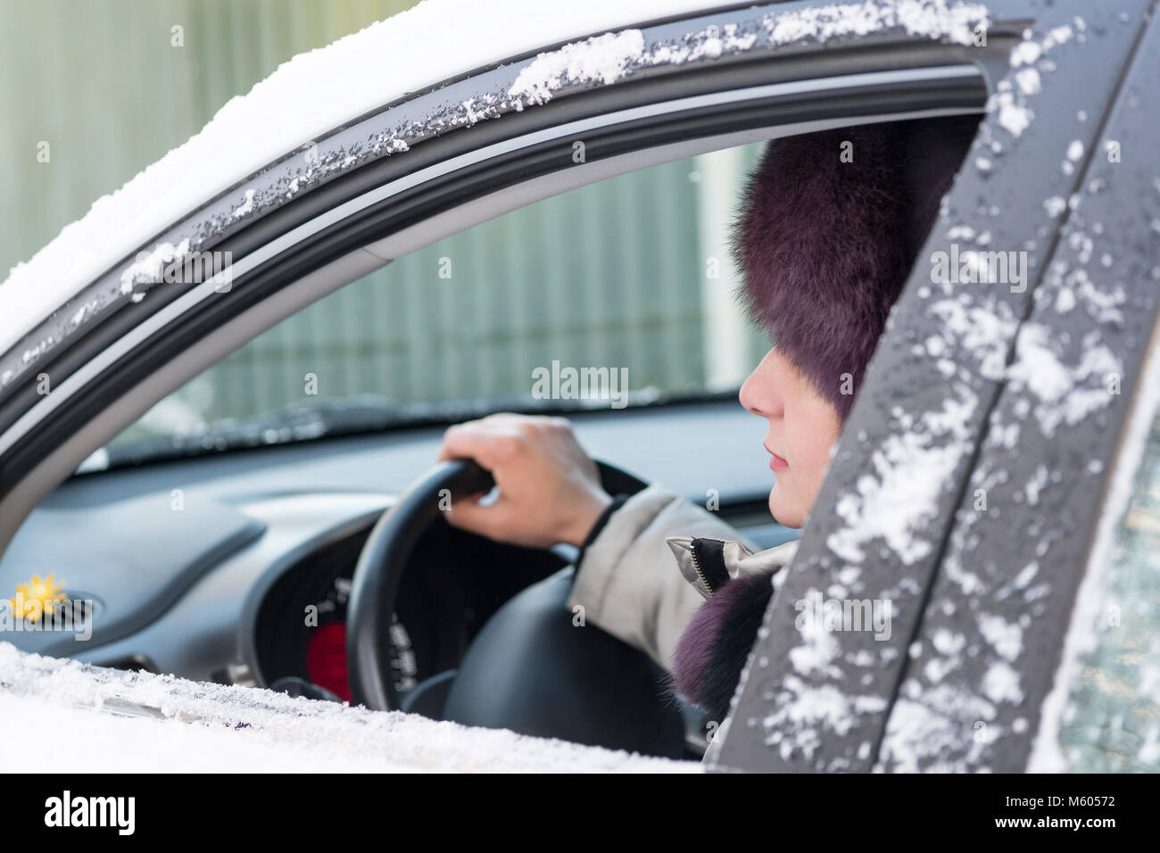 Das Mädchen sitzt am Steuer eines Autos. Im Fenster Öffnen des Profils der Frau und die Hand hält das Lenkrad. Tag, Winter. Stockfoto