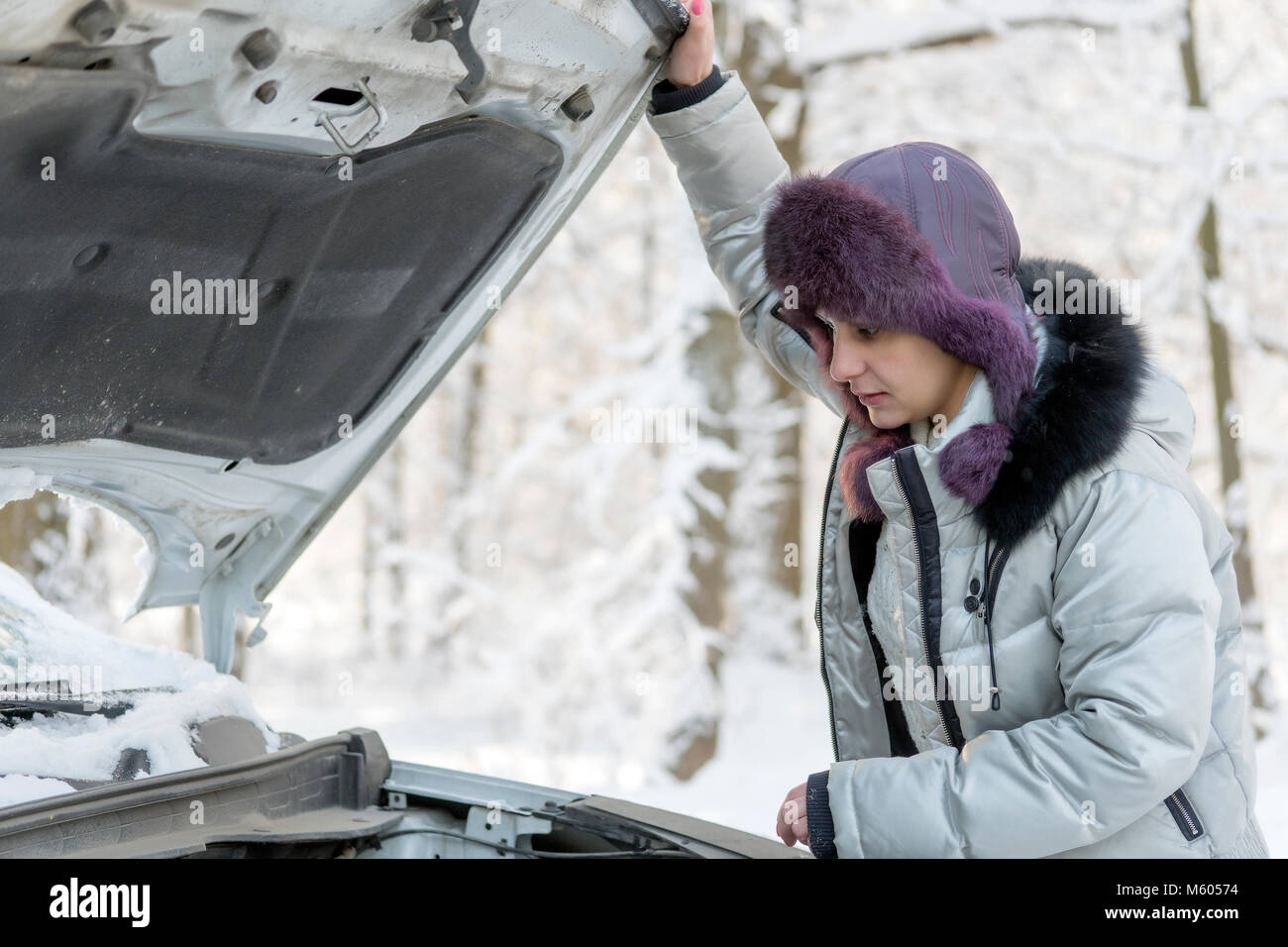 Das Mädchen hob die Haube vom Auto und schaut auf den Motor. Winter, Tag. Stockfoto